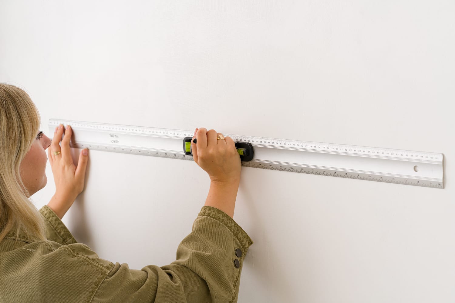 Using a ruler, a woman is measuring a wall as part of the process to install the wallpaper.