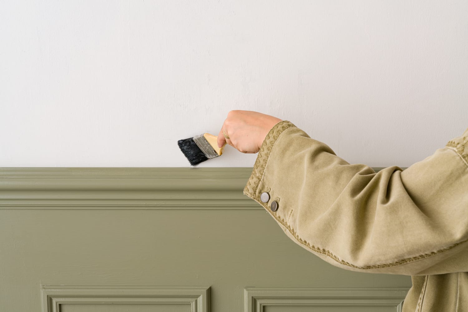 A woman is applying primer to a wall with a paintbrush as part of the process to install the wallpaper.