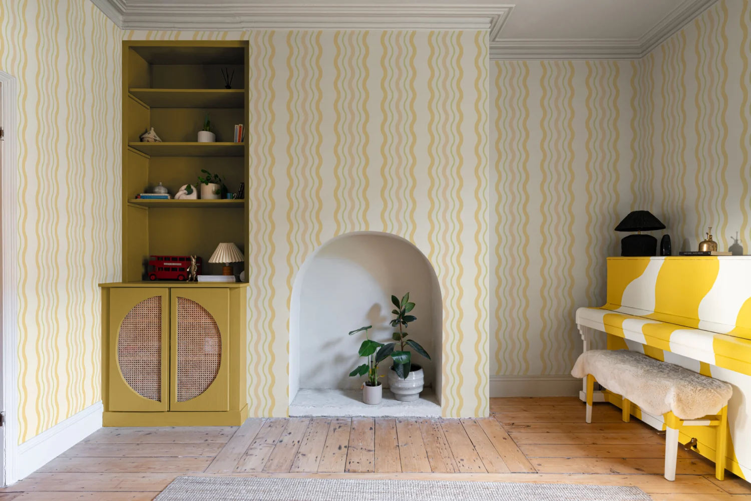 Living room with wavy yellow striped wallpaper, chartreuse built-in shelves, and a yellow-and-white painted piano.
