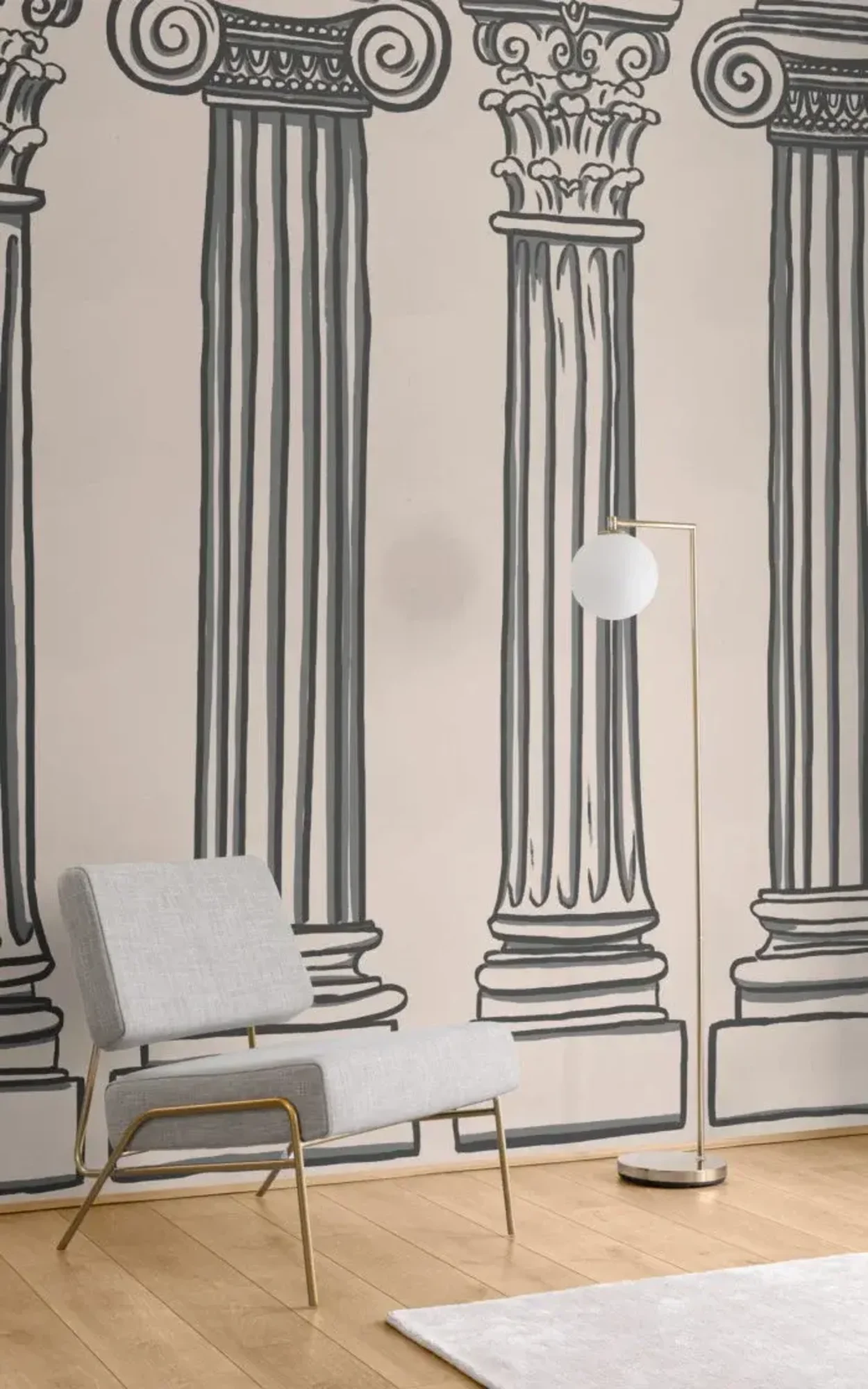A minimalist interior featuring a stylish gray fabric chair with golden legs, a modern floor lamp, and a striking wallpaper with bold black line drawings of classical columns on a cream background.