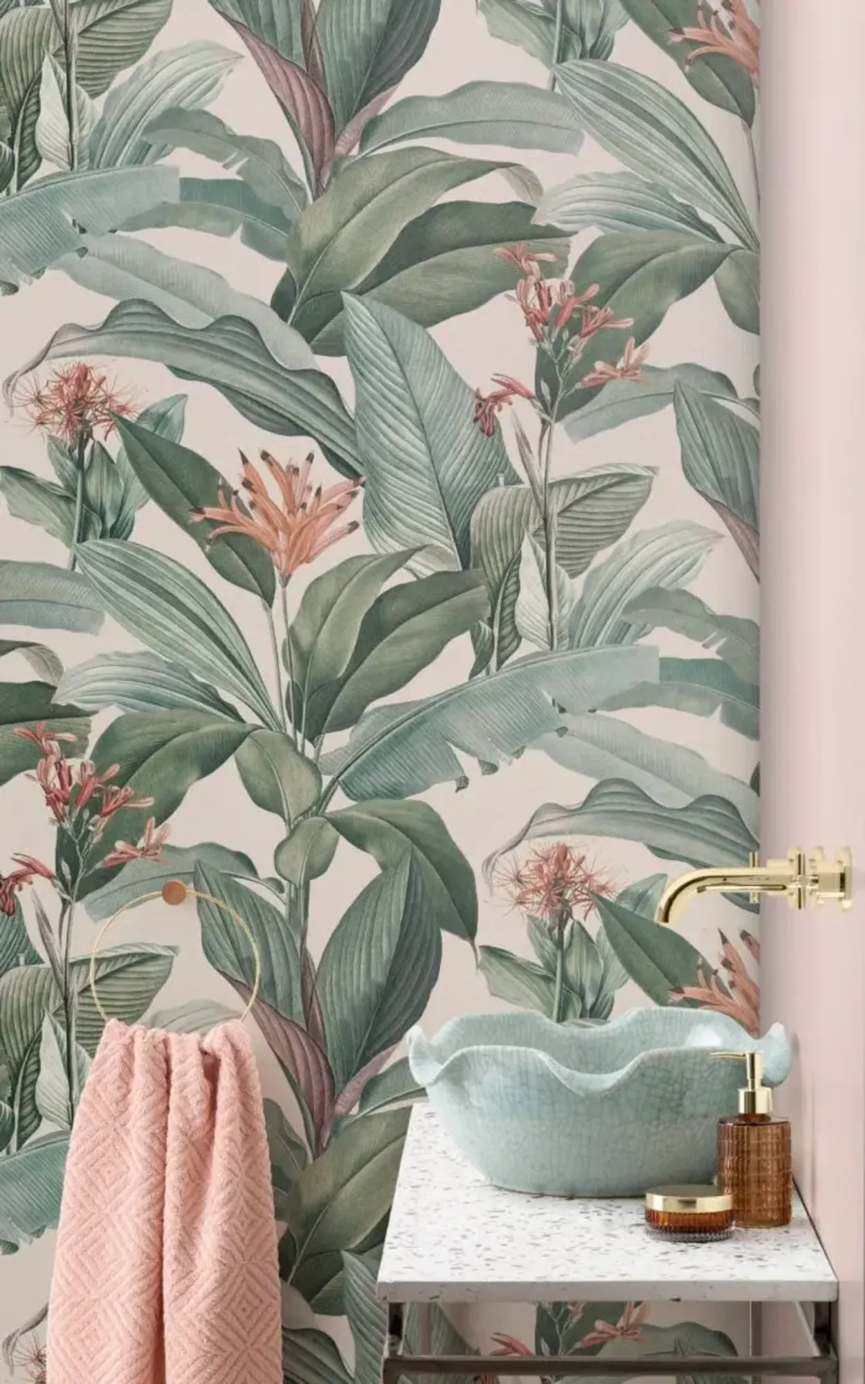  The bathroom features a botanical wallpaper with large, lush green leaves and soft pink accents, complemented by elegant gold fixtures and a minimalist basin, creating a serene and natural atmosphere.