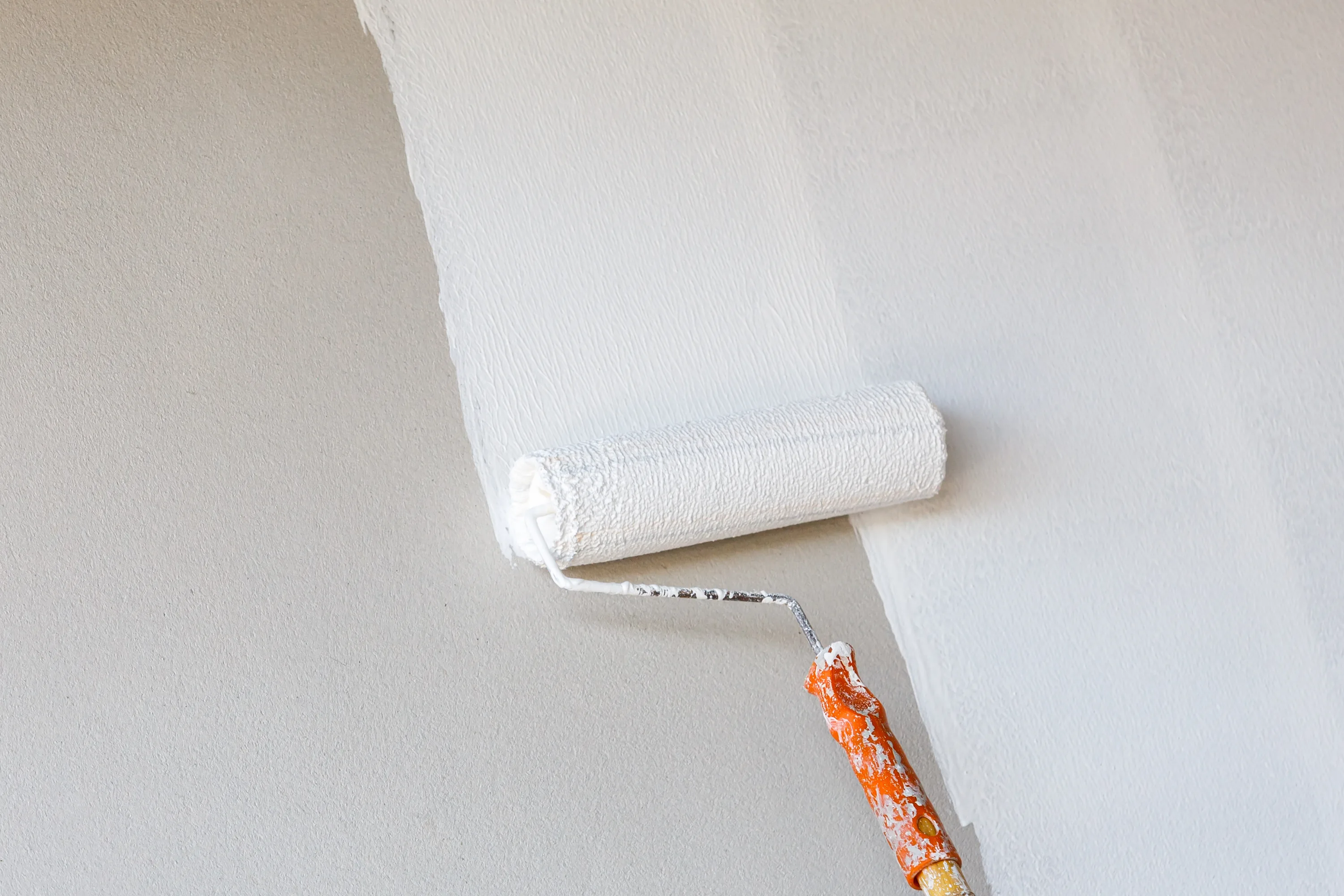 Primer being rolled onto a beige wall to create a smooth primed surface.