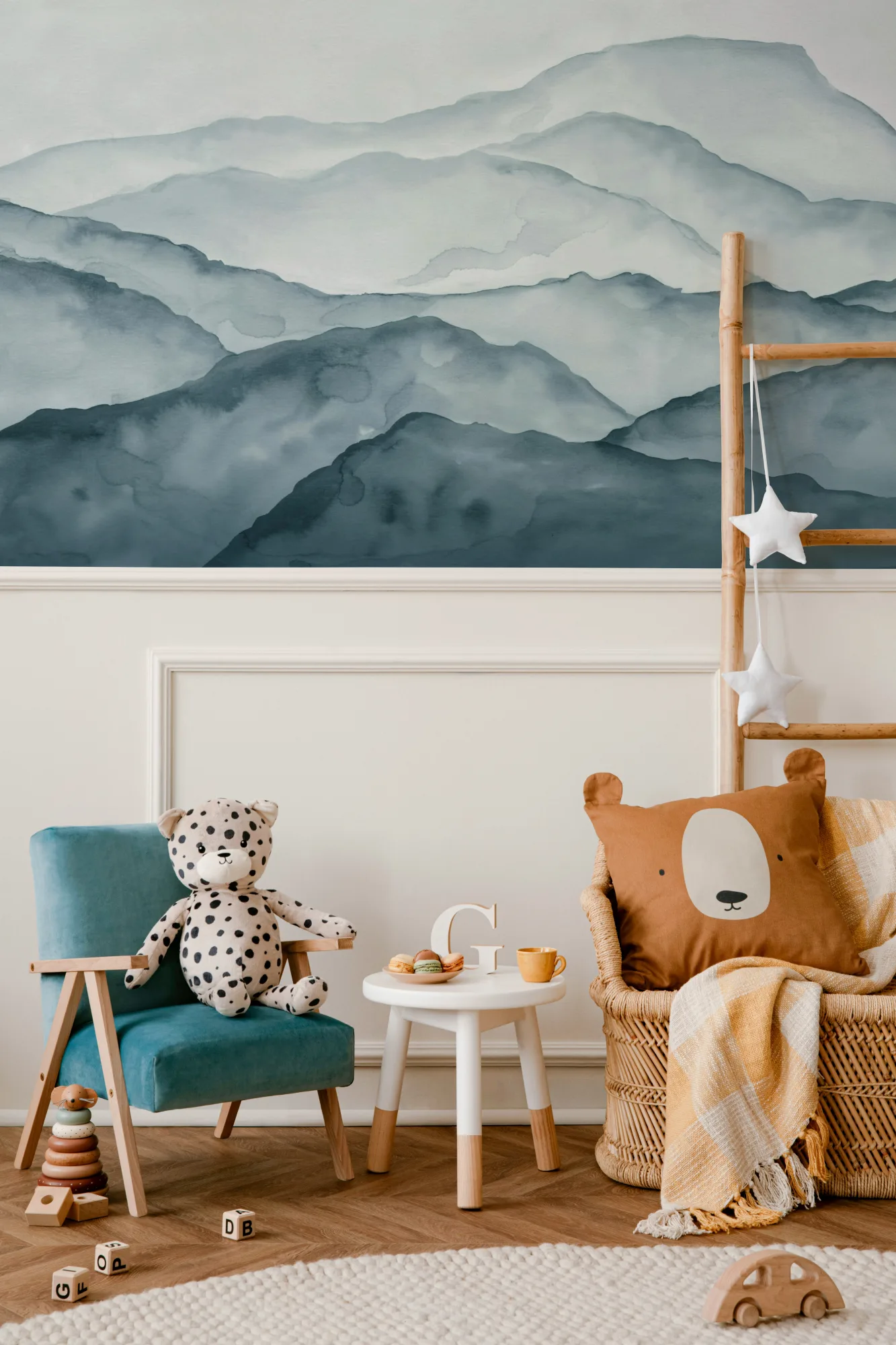 A soothing blue watercolor mountain mural in a kids' room with a teal chair, wicker basket, and cozy decor.