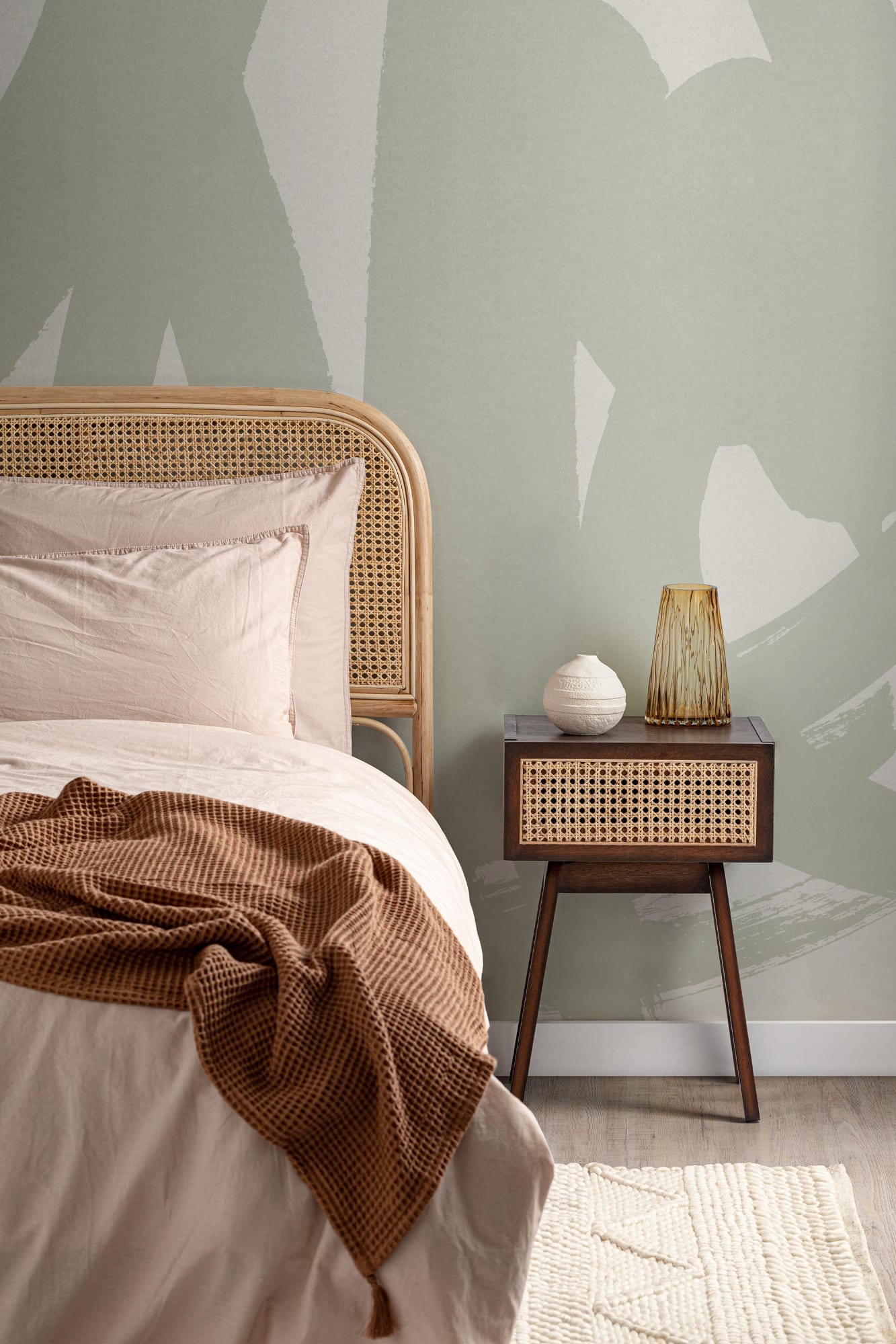 A calming minimalist bedroom with a green abstract mural, a rattan bed frame, and a natural wood nightstand.