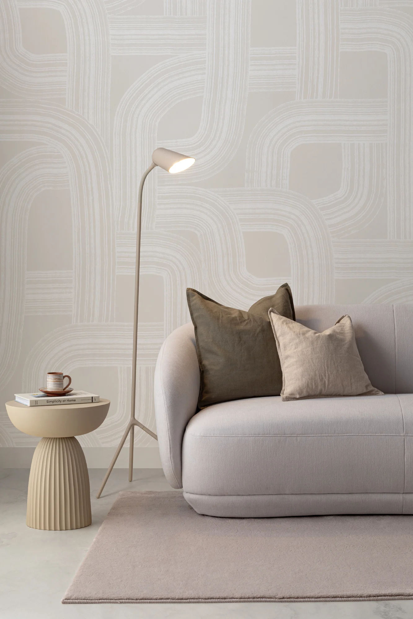 A minimalist living room with a neutral abstract wallpaper, soft curved furniture, and a sleek reading lamp.