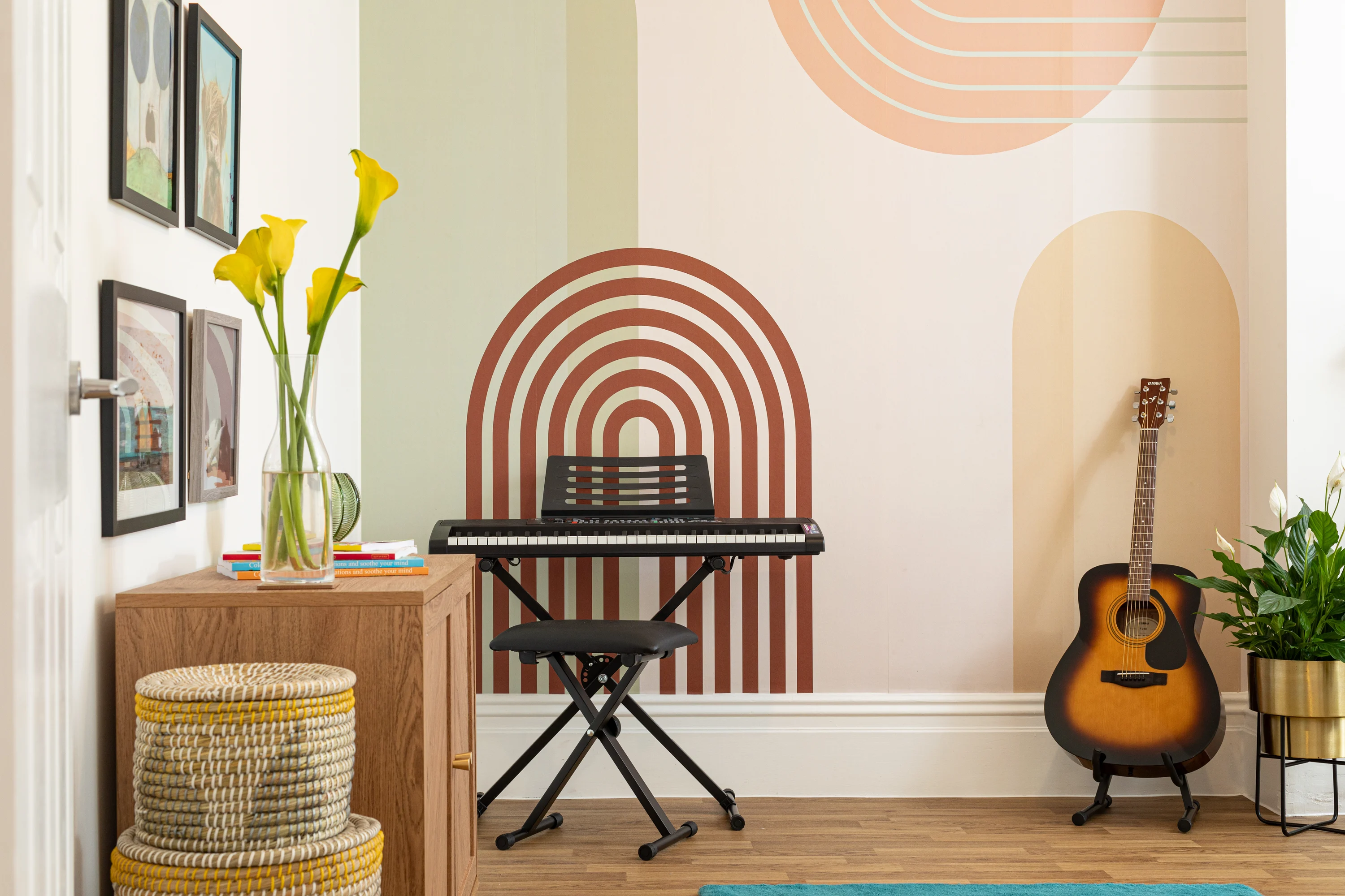 A keyboard and guitar sit in a music corner with a retro-style geometric mural in soft tones.