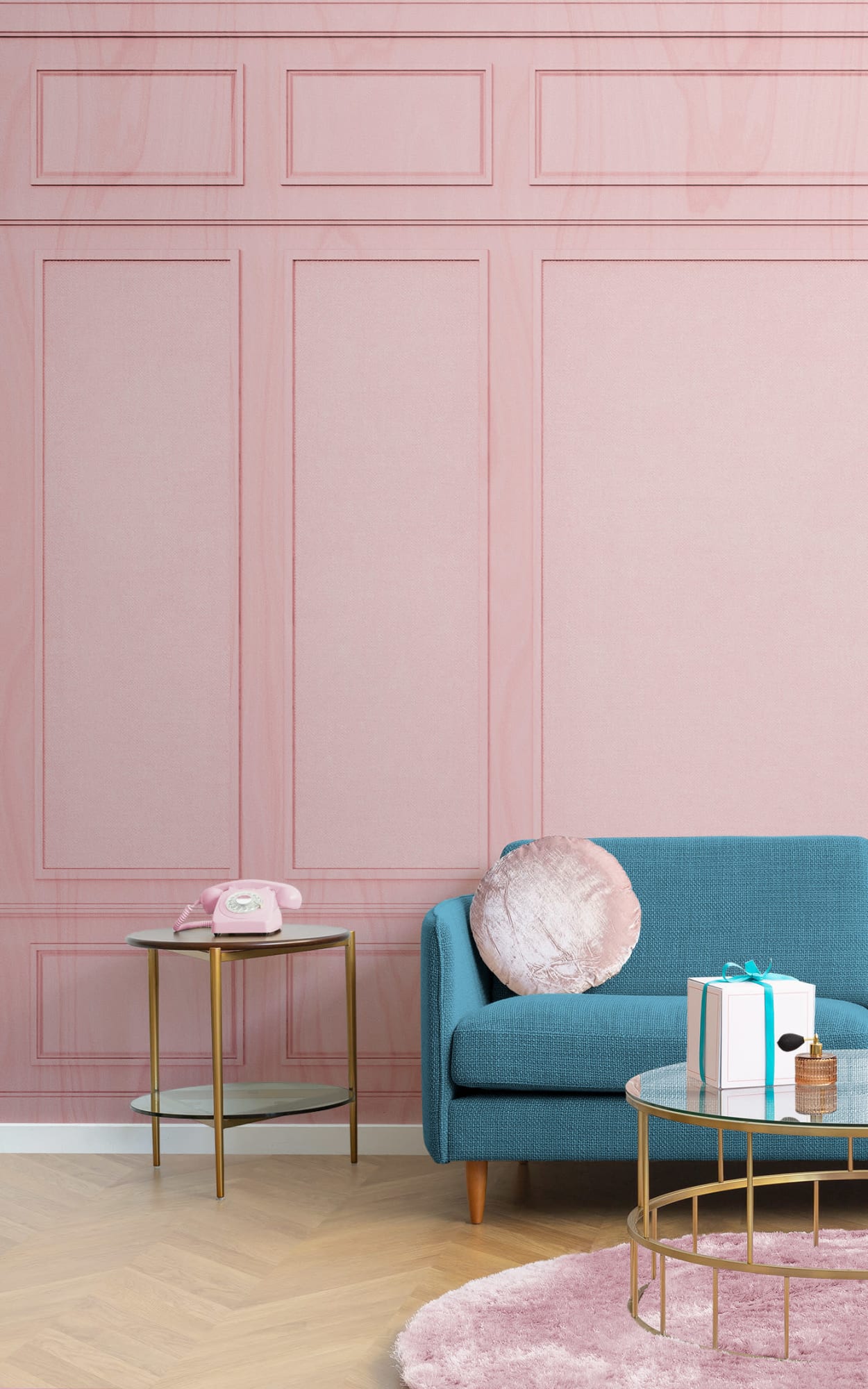A stylish living space with a pink paneled wall mural, featuring a teal blue sofa with a plush cushion, a small round gold and glass coffee table with a vintage pink telephone, and a pink round rug on a light wooden floor.