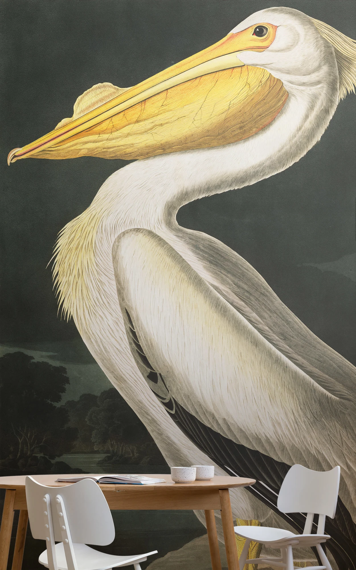 A dining area with a large wall mural of a detailed illustration of a pelican. The space includes a wooden table with simple white chairs and small ceramic bowls.