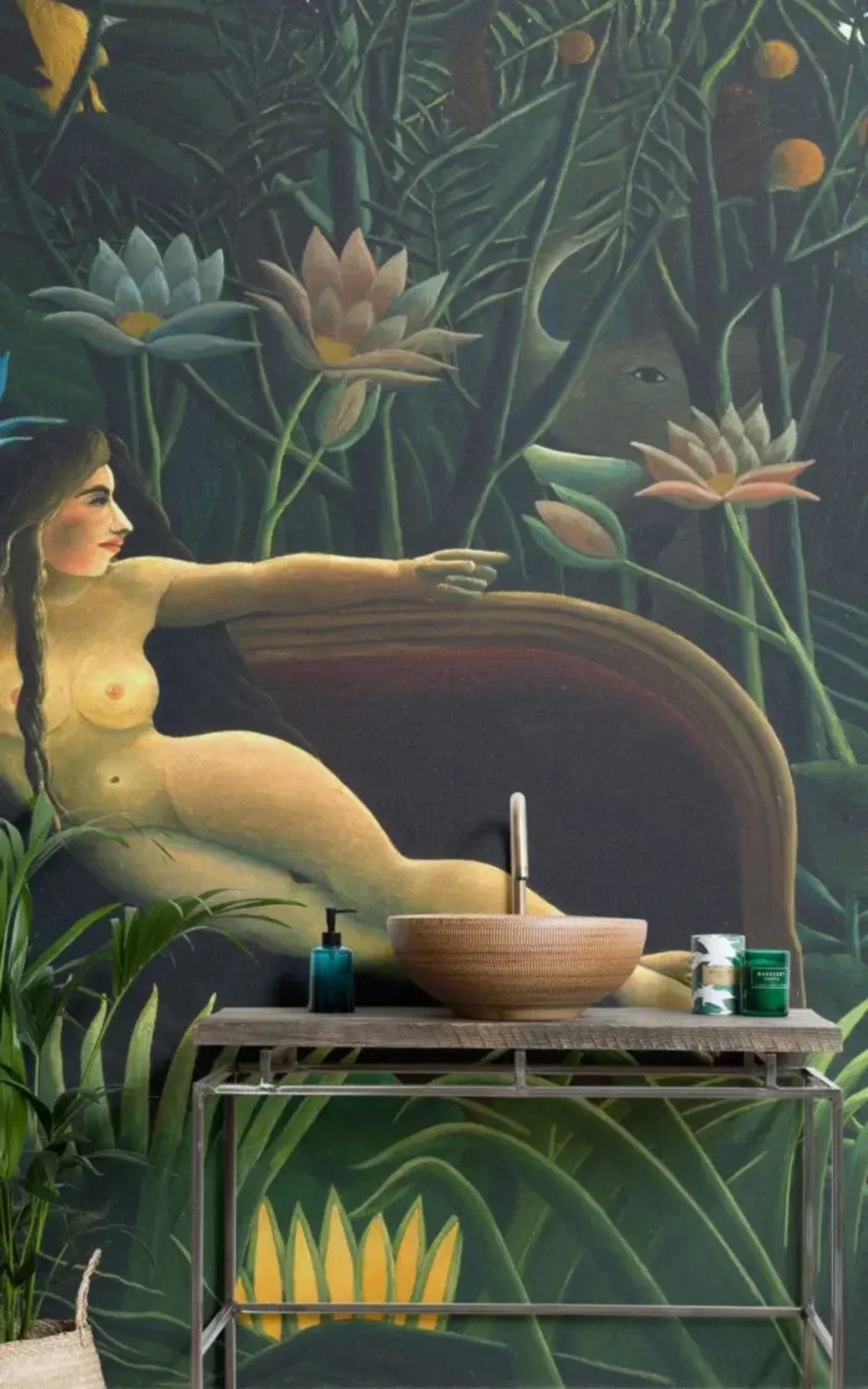  A bathroom featuring a rustic washstand with a large bowl sink, adorned by an art nouveau-style mural of a reclining nude surrounded by lush, exotic plants and flowers, which creates a captivating and immersive backdrop that combines art with nature.