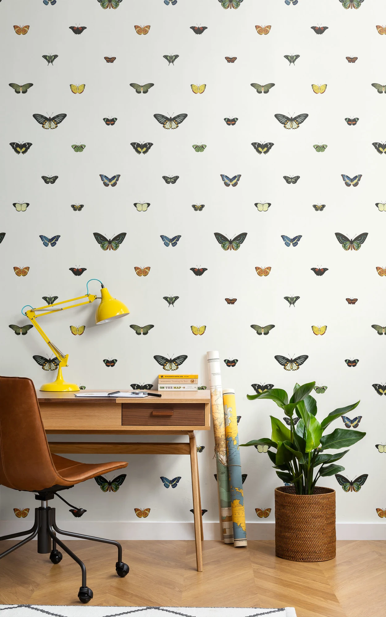 A bright and cheerful workspace featuring a white mural with colorful butterfly illustrations, with a stylish mid-century modern desk, a yellow desk lamp, and a lush potted plant beside it.