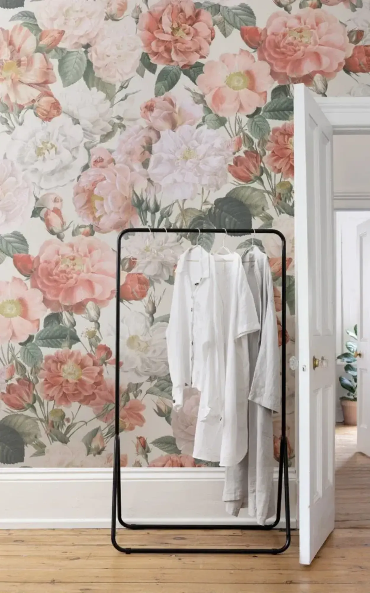 This room features a large, beautifully detailed floral wallpaper that adds a touch of elegance and softness, perfectly complementing the minimalistic and modern clothing rack with neatly hung white garments.