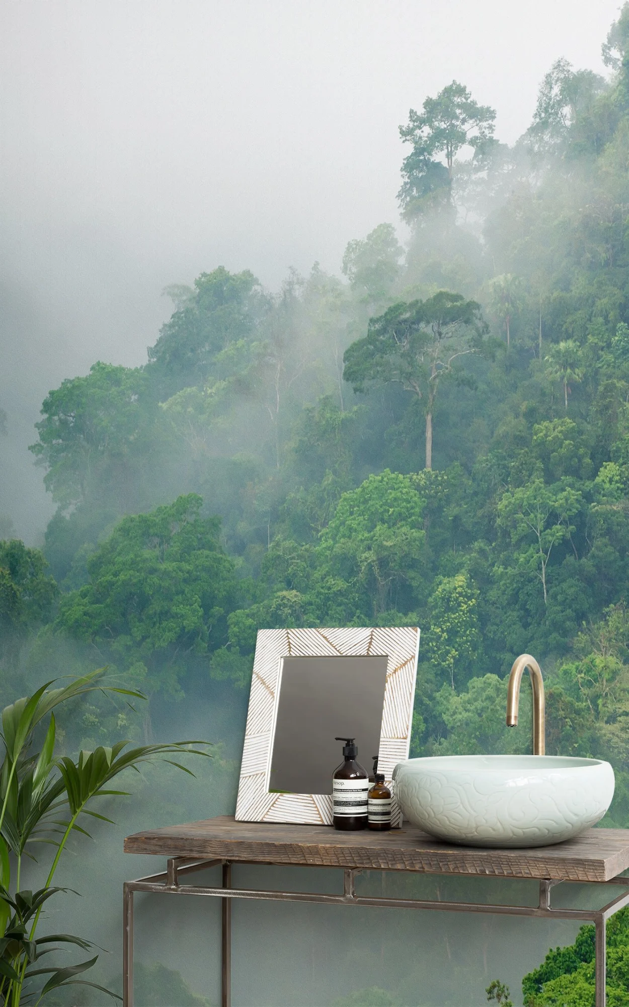 Elegant bathroom vanity featuring a rustic table with a white patterned vessel sink, framed mirror, and toiletry bottles, set against a lush, misty rainforest backdrop.