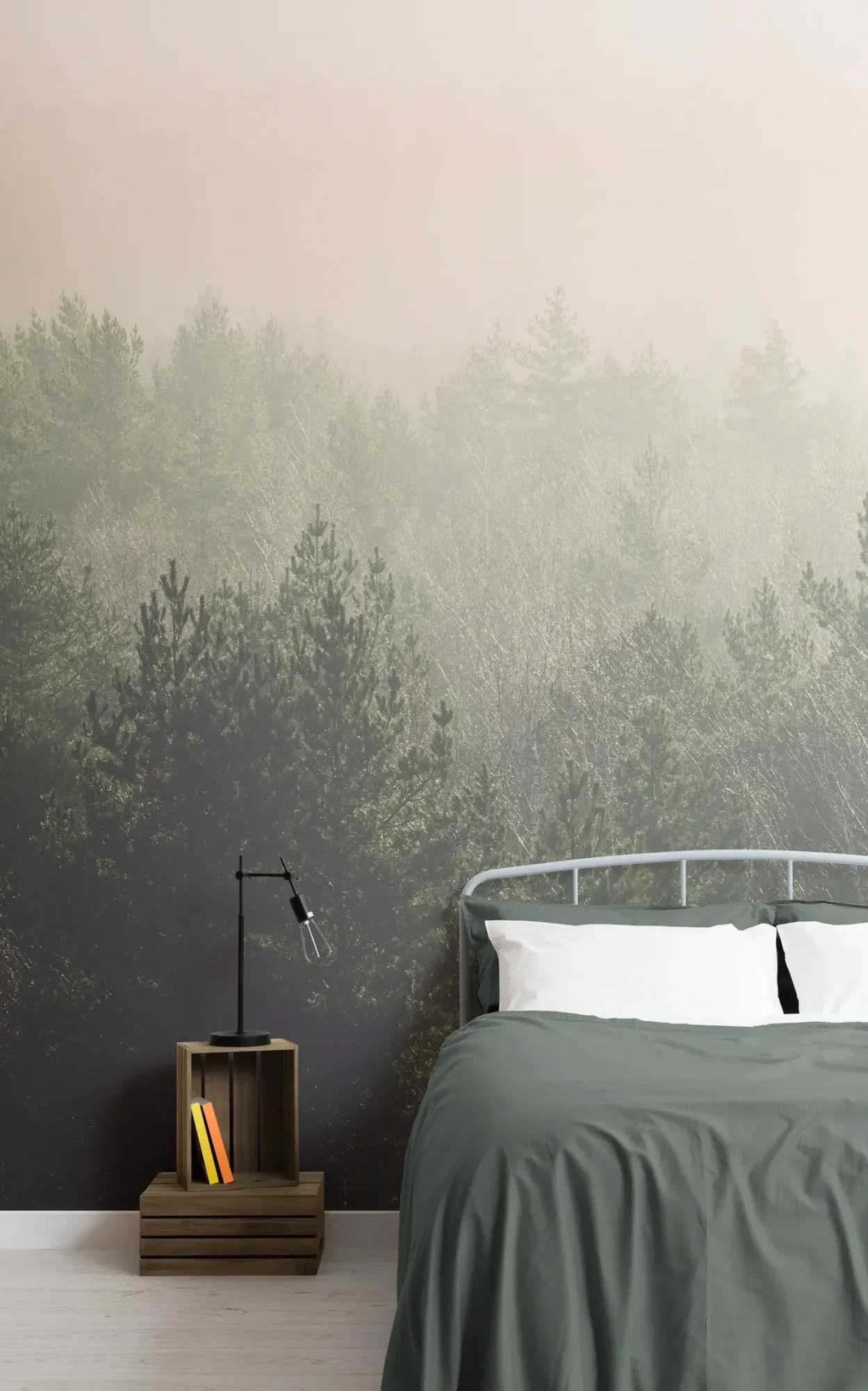 Cozy bedroom corner featuring a bed with dark green bedding, a simple wooden bedside table with books and a black lamp, set against a large wall mural of a foggy pine forest.