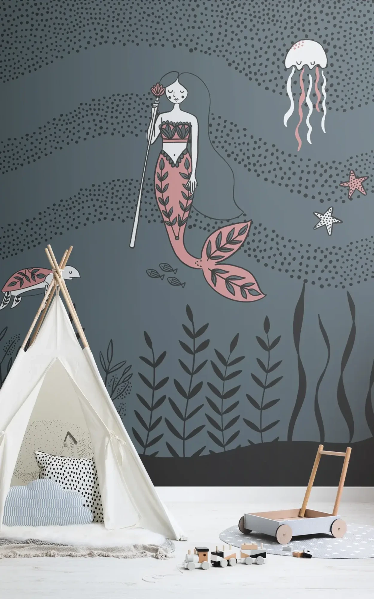 A child's play area with a teepee and wooden toys on a light gray rug, against a wall mural featuring a stylized mermaid, jellyfish, turtle and underwater plants in a dark sea-themed background.