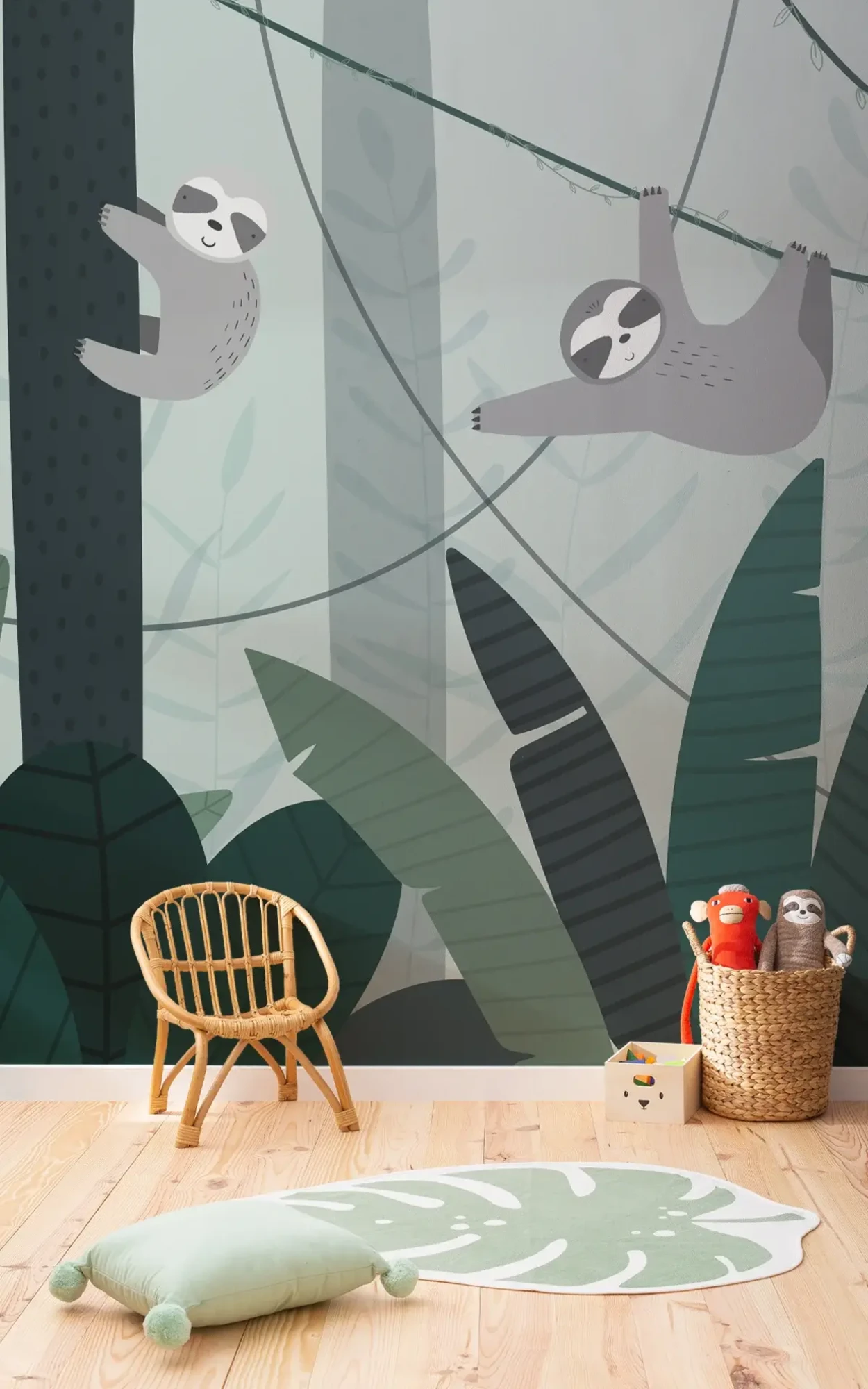  A children's room corner with a playful wall mural of sloths hanging from vines, complemented by a rattan chair, a basket of stuffed animals, and a green leaf-shaped rug on a wooden floor.