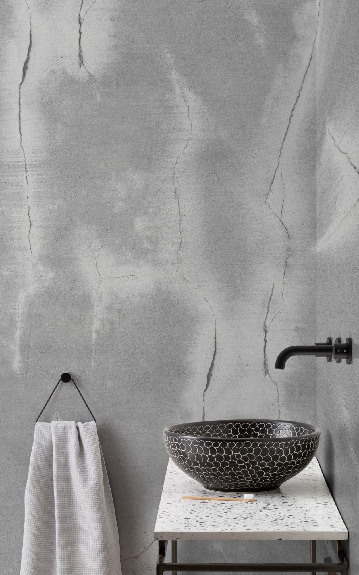 Modern bathroom with cracked concrete effect wall, terrazzo countertop, and black patterned sink bowl.