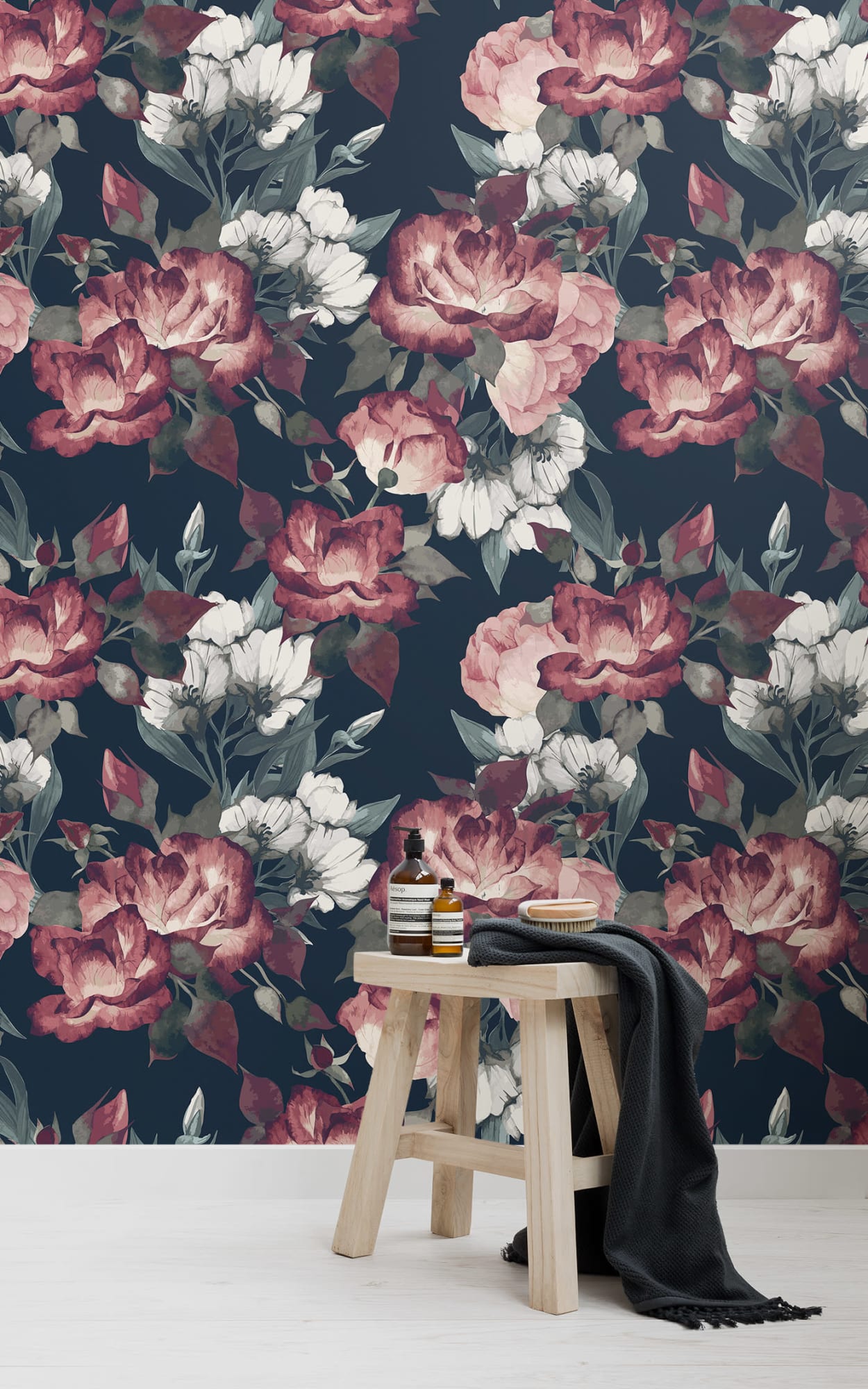 Bathroom with dark floral wallpaper, wooden stool, skincare products, and black towel.