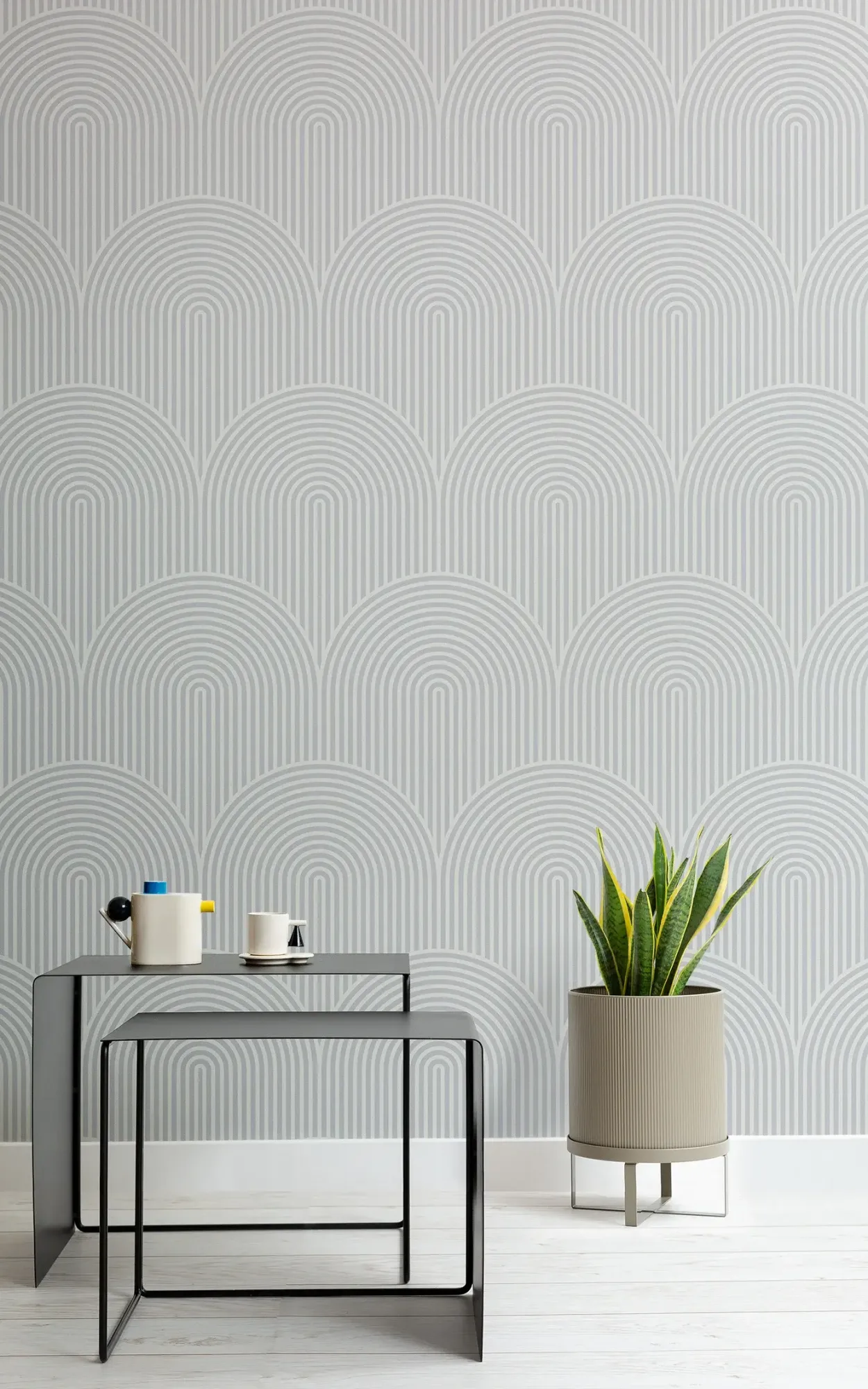 A minimalist interior design with a grey geometric patterned wallpaper, featuring a sleek black metal console table and a beige plant pot with a green snake plant.
