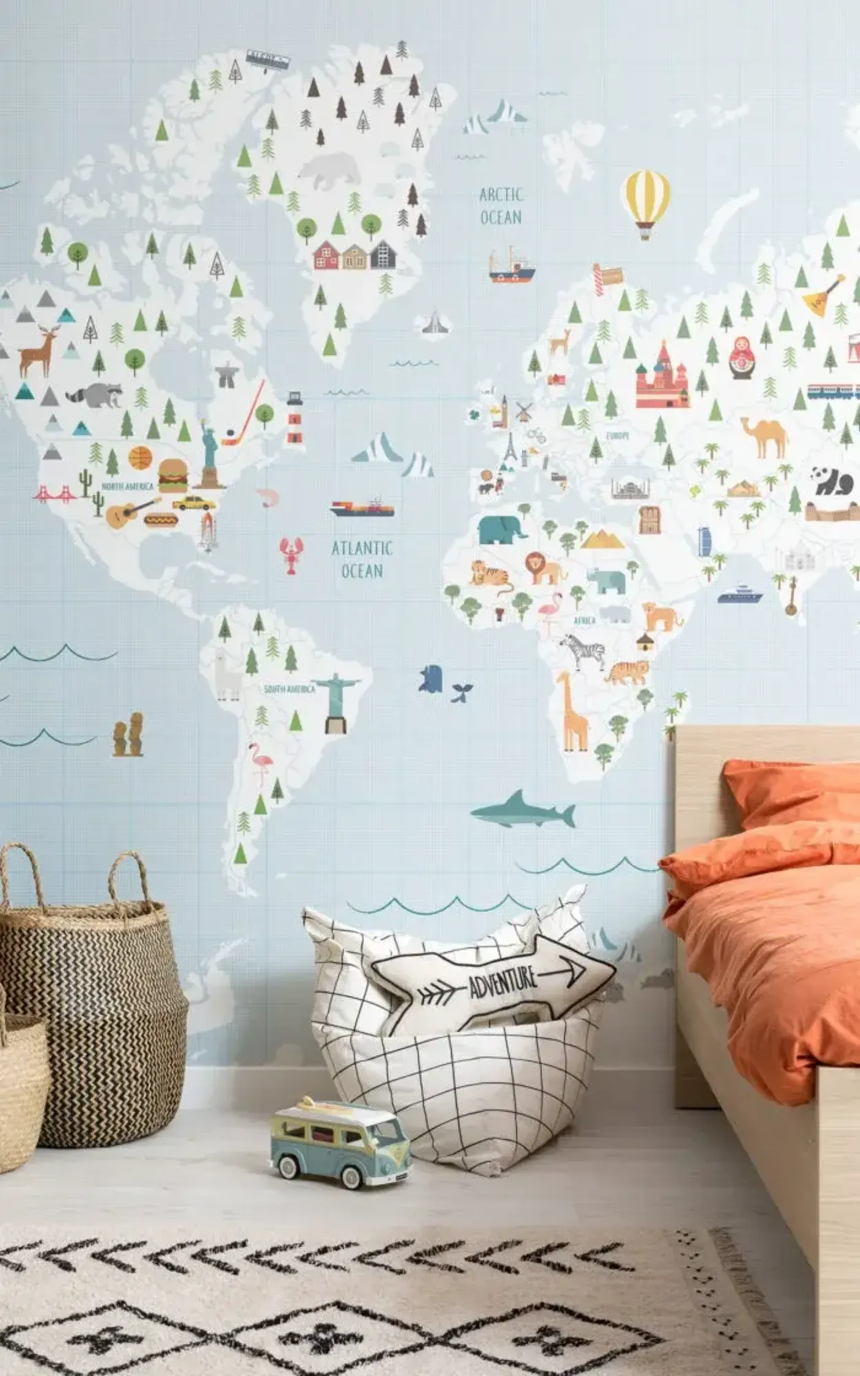A children's bedroom featuring a wall covered in a playful and educational world map wallpaper, with a wooden bed, an 'adventure' bean bag, a toy van, and a patterned rug, creating a themed exploration space.