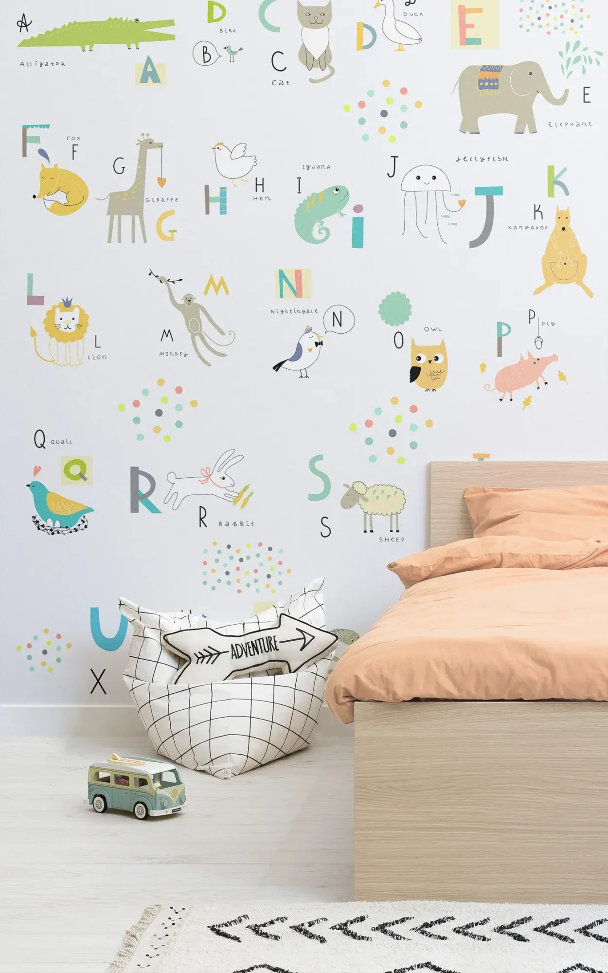 A playful and educational children's bedroom featuring a wall adorned with alphabet-themed animal illustrations, accompanied by a wooden bed with peach bedding, a patterned rug, a 'adventure' bean bag, and a toy van on the floor.