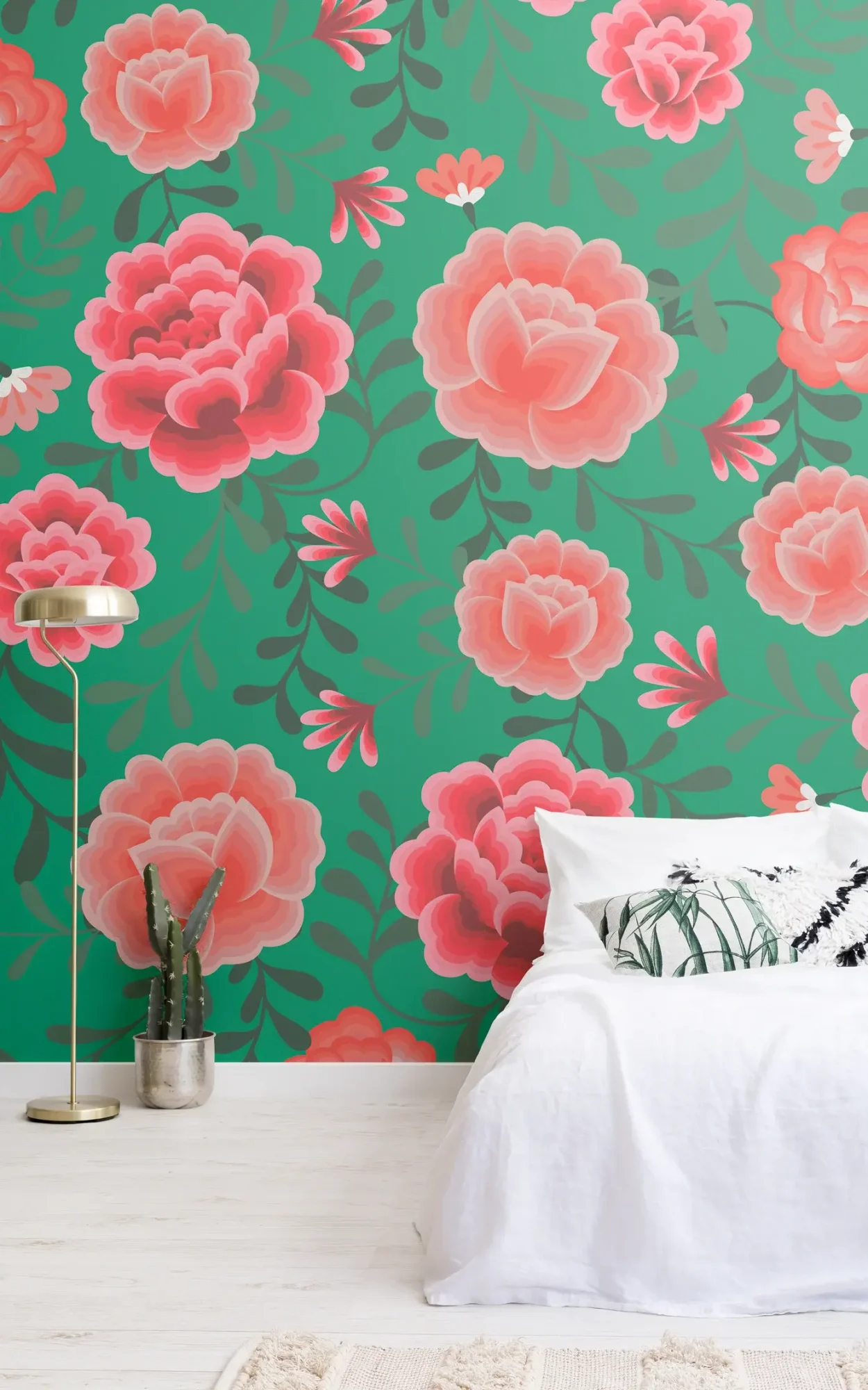 A tranquil bedroom setting with a white bed, a decorative pillow, and a floor lamp beside a potted cactus, against a backdrop of a green floral wallpaper adorned with large pink roses.