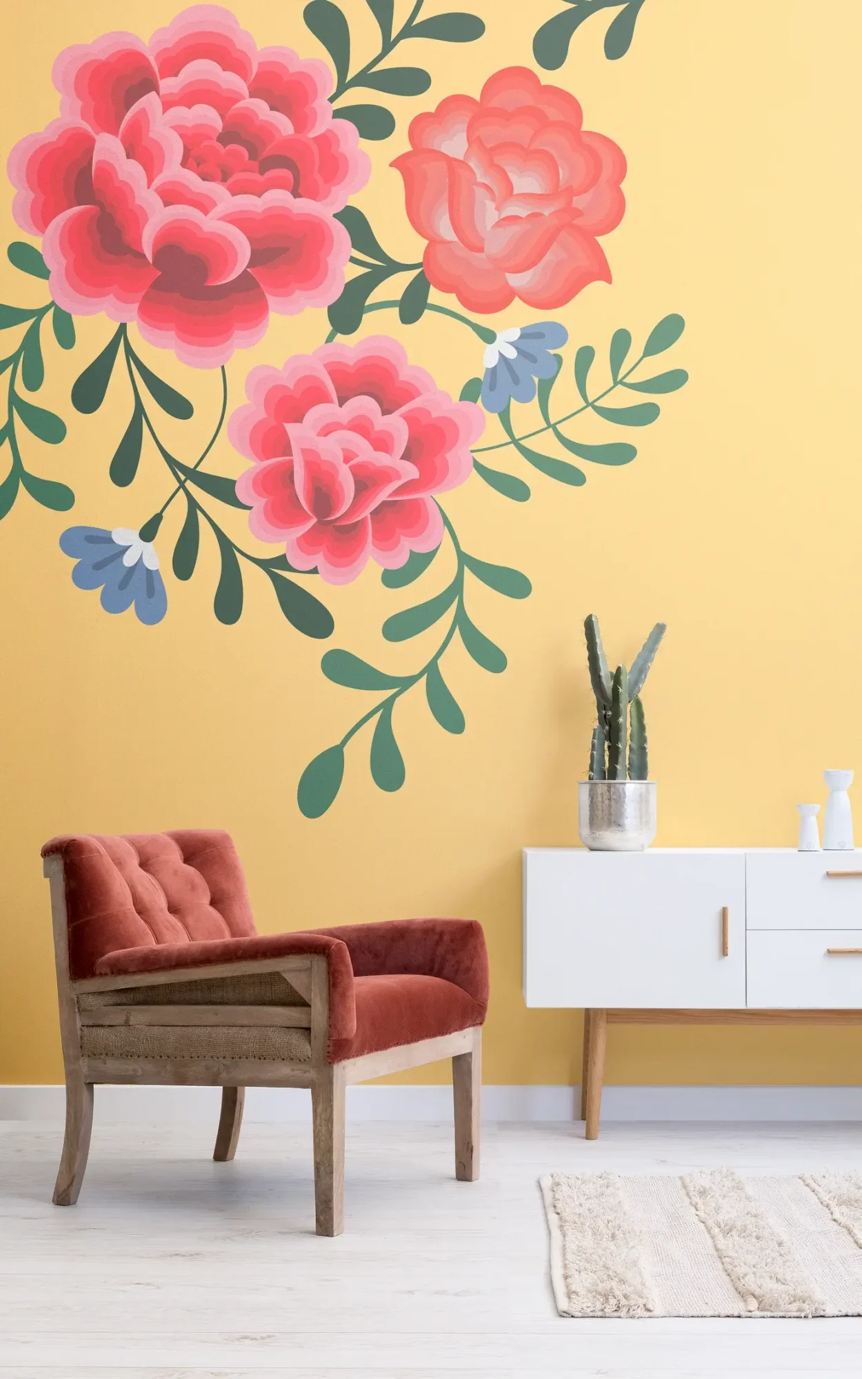 A cozy room featuring a large floral mural with pink and red roses on a yellow wall, complemented by a red velvet armchair, a white modern sideboard, and a cactus plant.