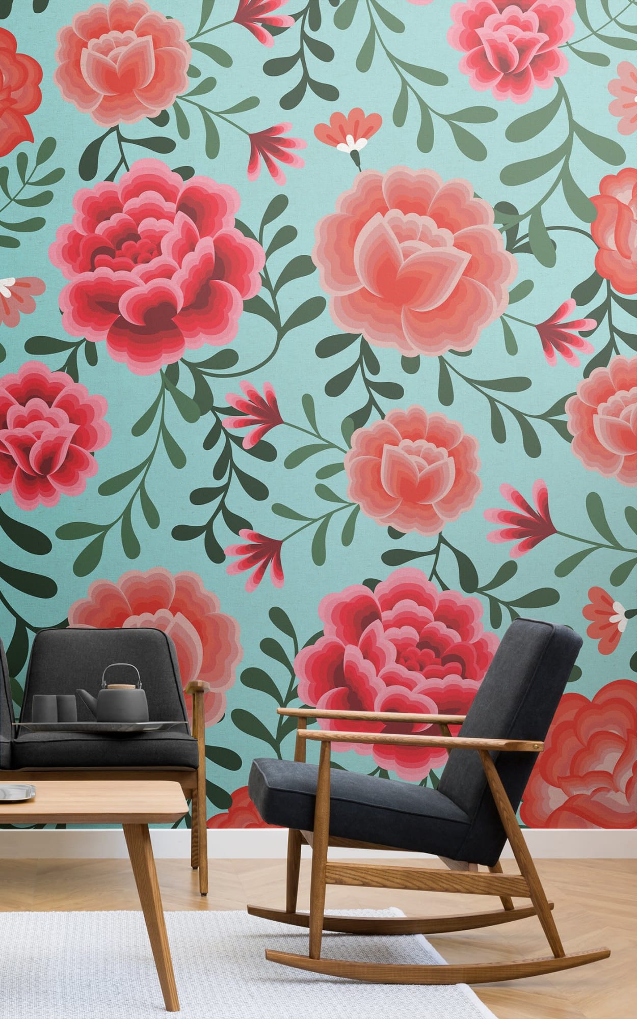 A modern living room featuring a dark gray rocking chair and a wooden coffee table against a light teal backdrop decorated with large red and pink floral patterns.