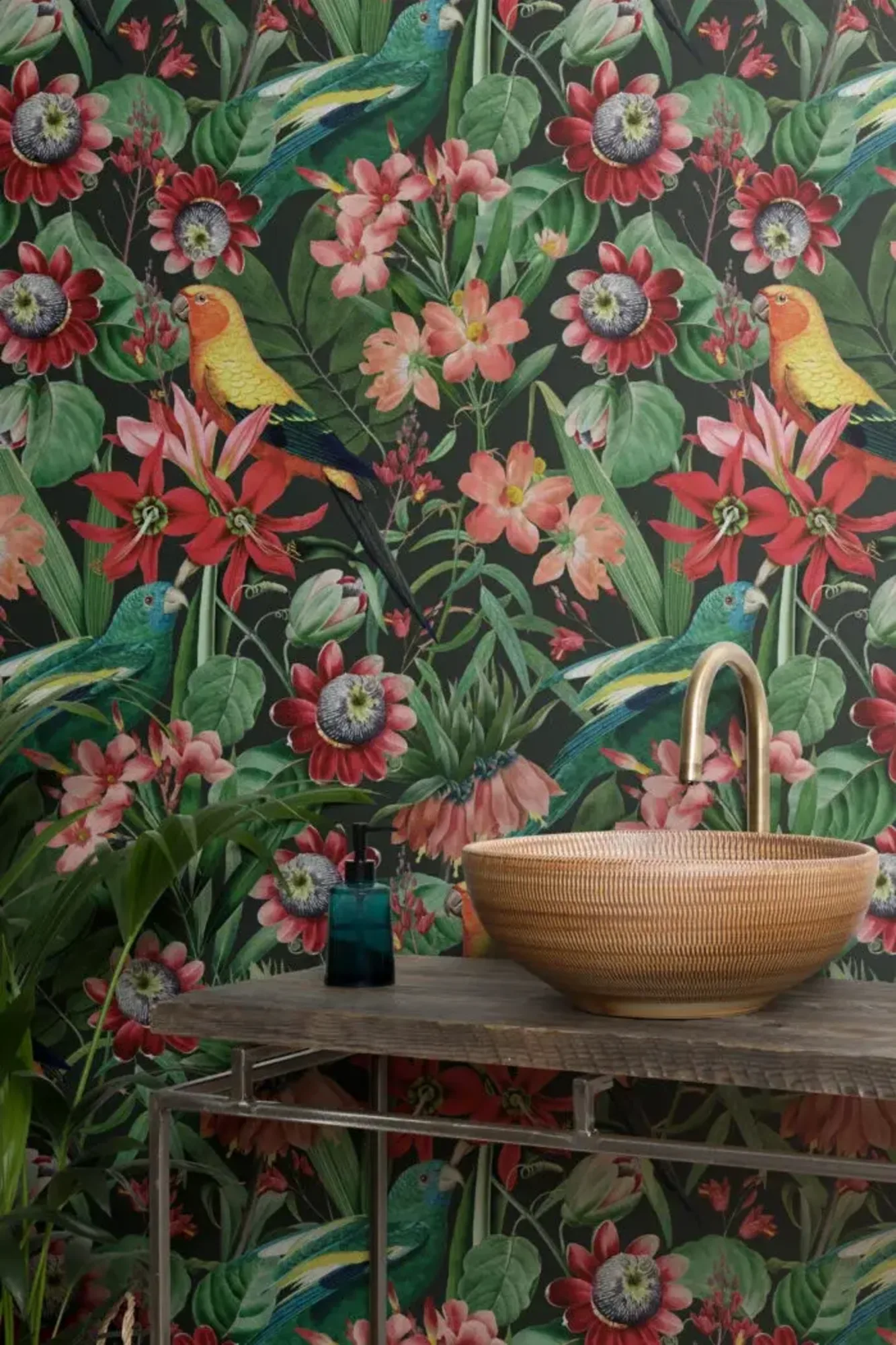 A vividly detailed tropical scene on wallpaper, featuring colorful parrots and lush floral elements, complemented by a rustic bathroom vanity with a woven basket and a decorative blue bottle.