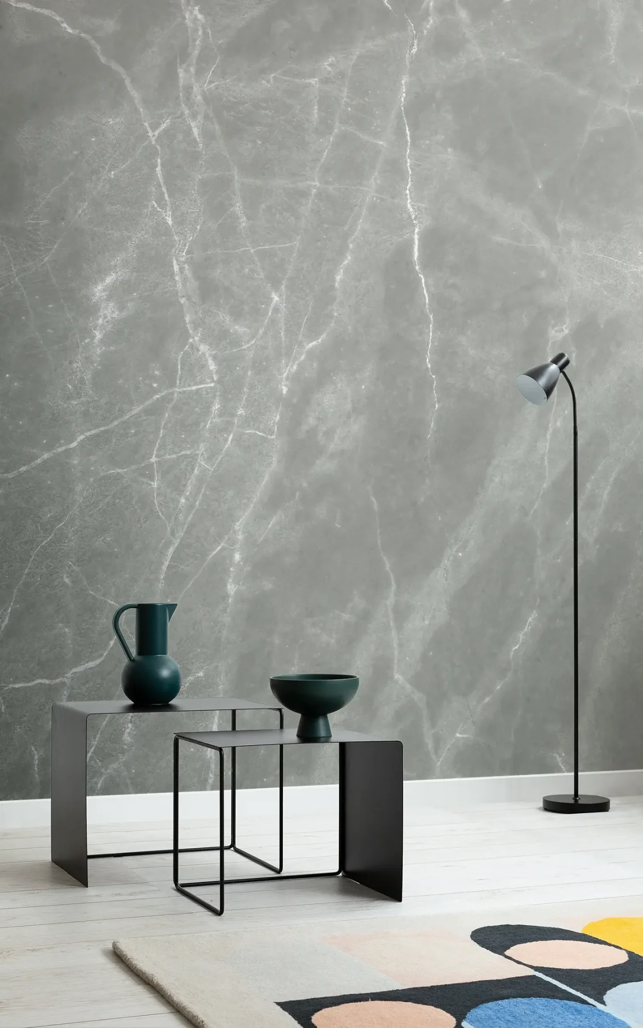  A modern living room features two black metal tables with dark green decor, a black floor lamp, and a gray marble wall mural behind.