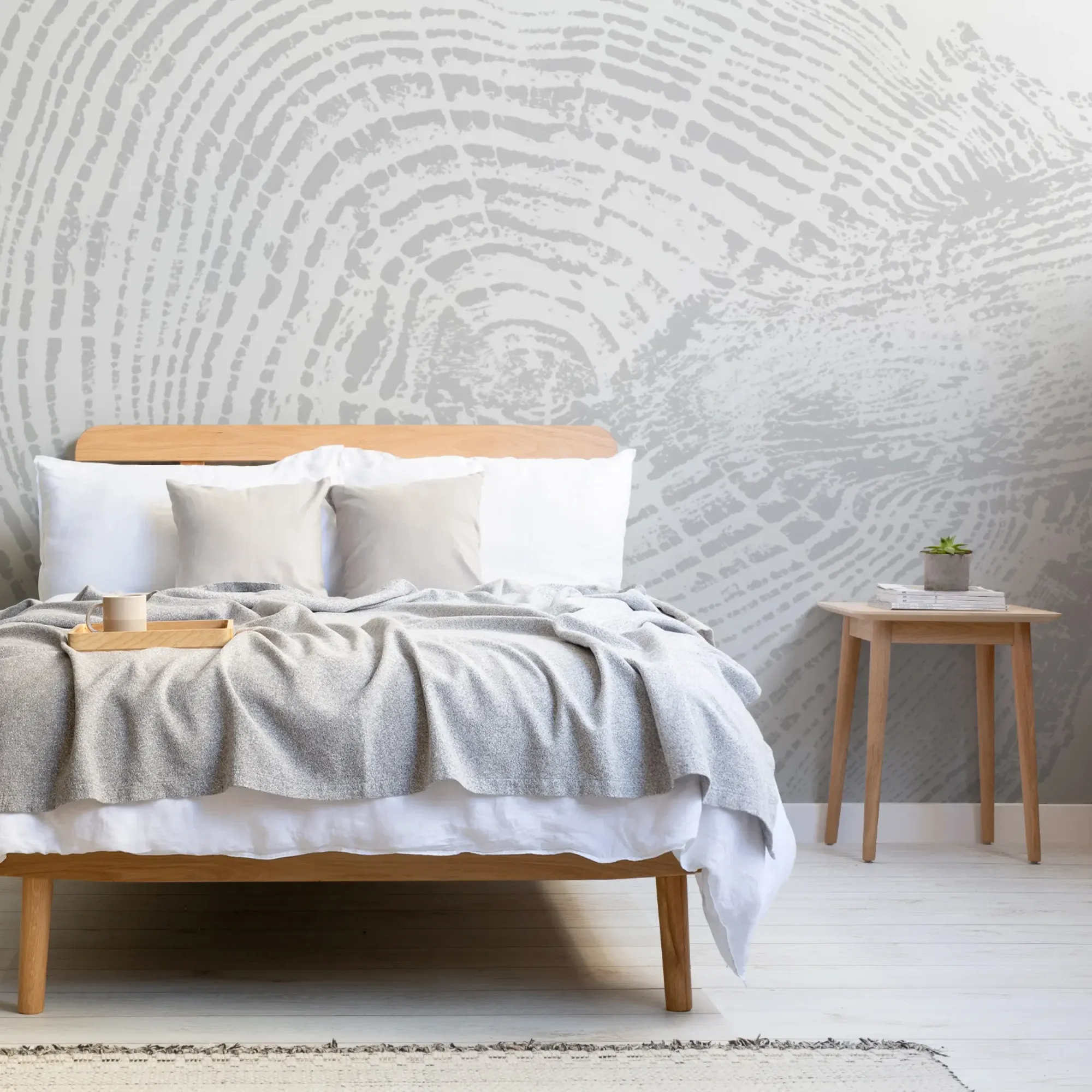 A modern bedroom features a wooden bed with white and gray bedding, a wooden side table, and a light gray wood print mural on the wall behind.