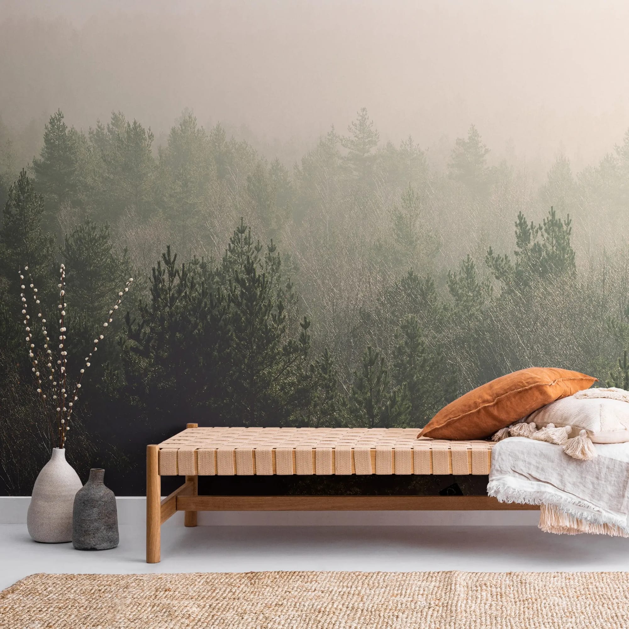  A minimalist living room features a woven bench with pillows and a blanket, decorative vases, and a mural of a misty forest on the wall behind.