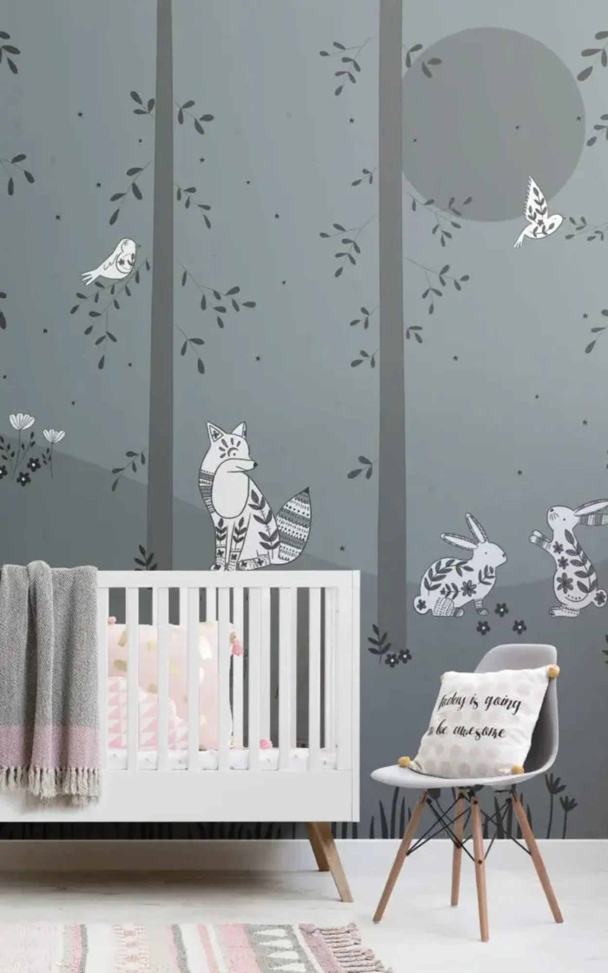 A children's room features a white crib, a chair with a cushion, a patterned rug, and a mural of a whimsical forest with foxes, bunnies, and birds on the wall behind.