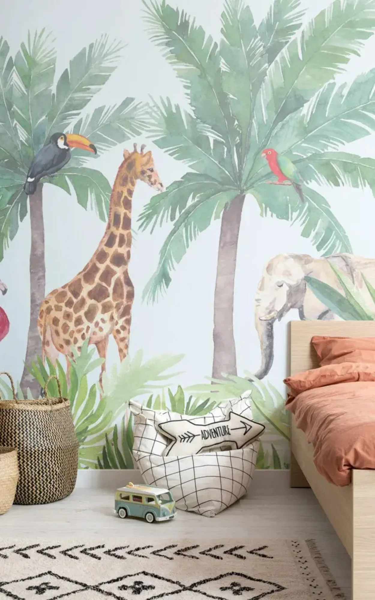 A children's bedroom features a jungle-themed mural with palm trees, a giraffe, an elephant, and birds, along with a bed, woven baskets, and a toy van on the floor.