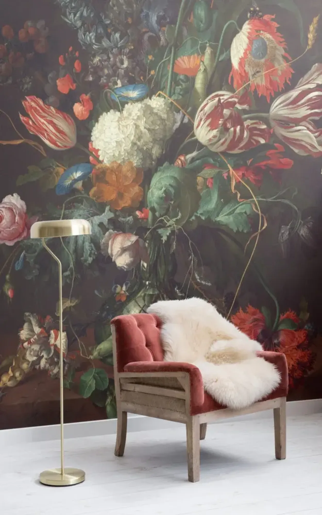 A cozy living space features an orange tufted armchair with a white fur throw, a gold floor lamp, and a dramatic floral mural as the backdrop.