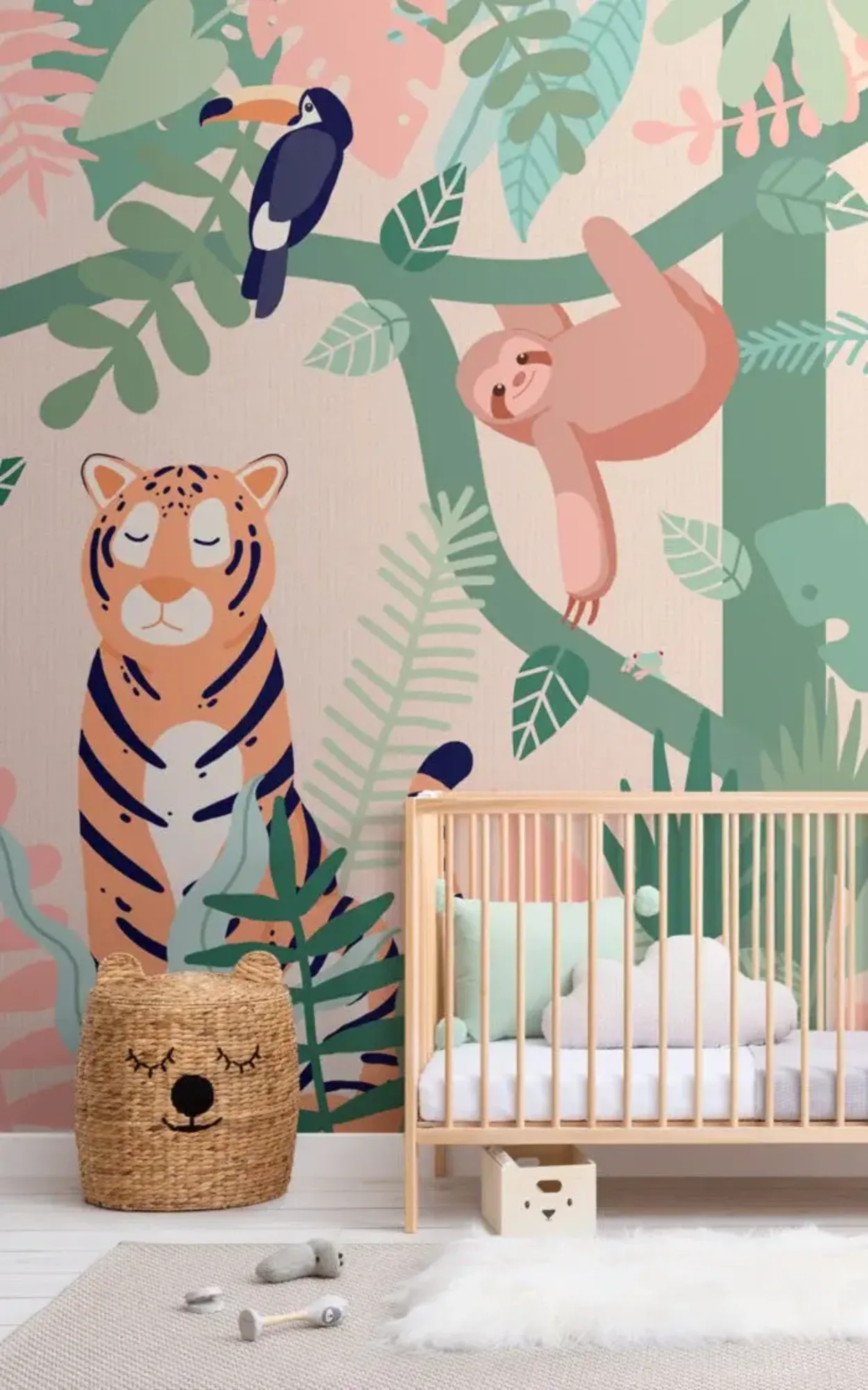 A nursery features a wooden crib with pastel cushions, a woven basket, and a colorful jungle mural with a tiger, sloth, and toucan on the wall.