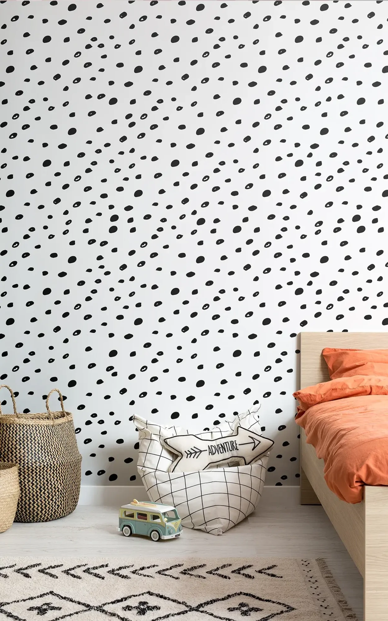  A child's bedroom features a bed with orange bedding, woven storage baskets, a play area with toys, and a wall with black speckled wallpaper.
