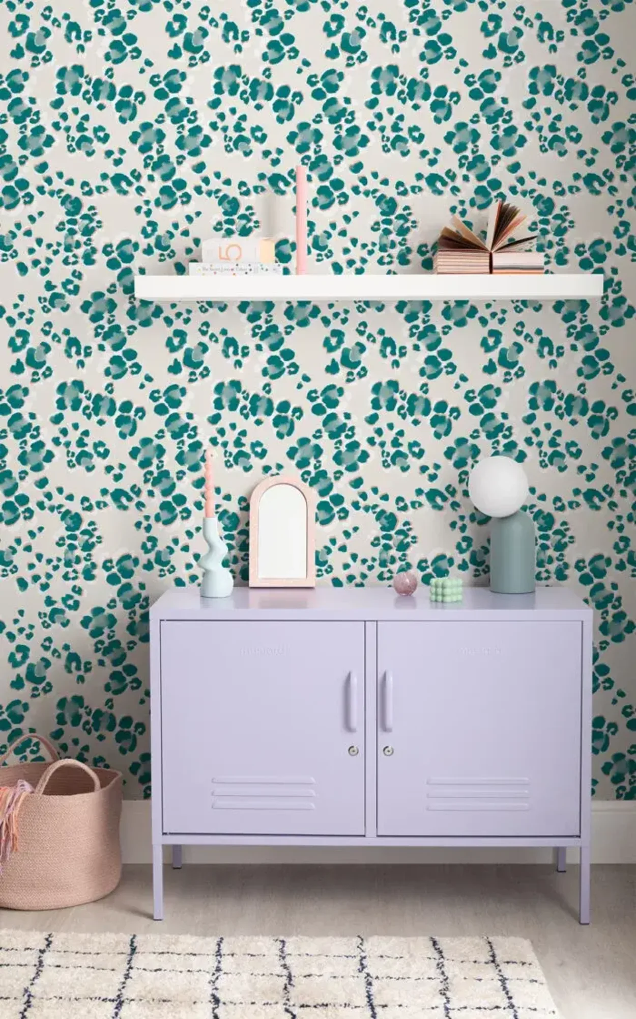  A stylish room features a light purple cabinet, a floating shelf with decor items, and a wall with teal leopard print wallpaper.