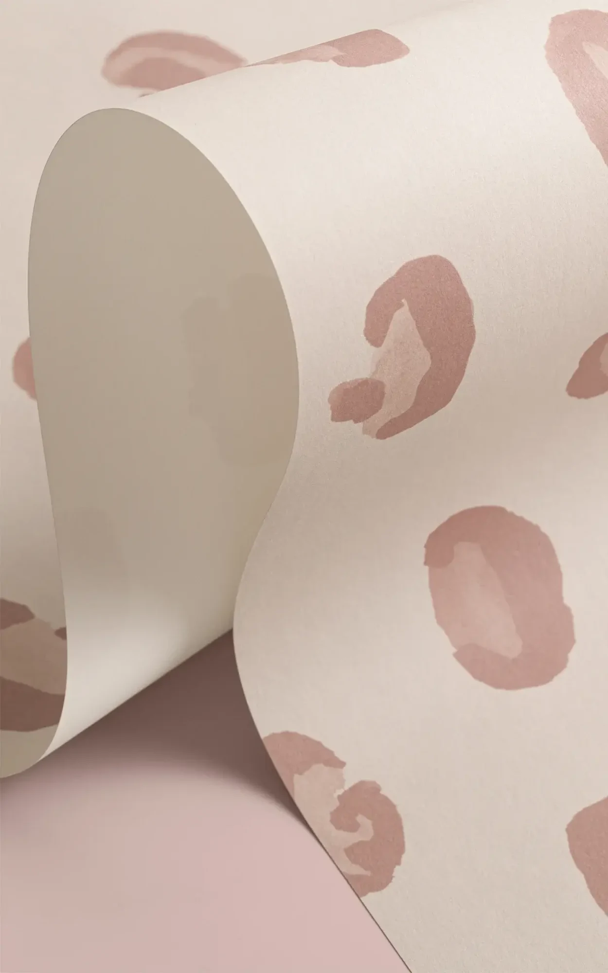 A roll of wallpaper with a light beige background and pink leopard spots is displayed against a pink surface.