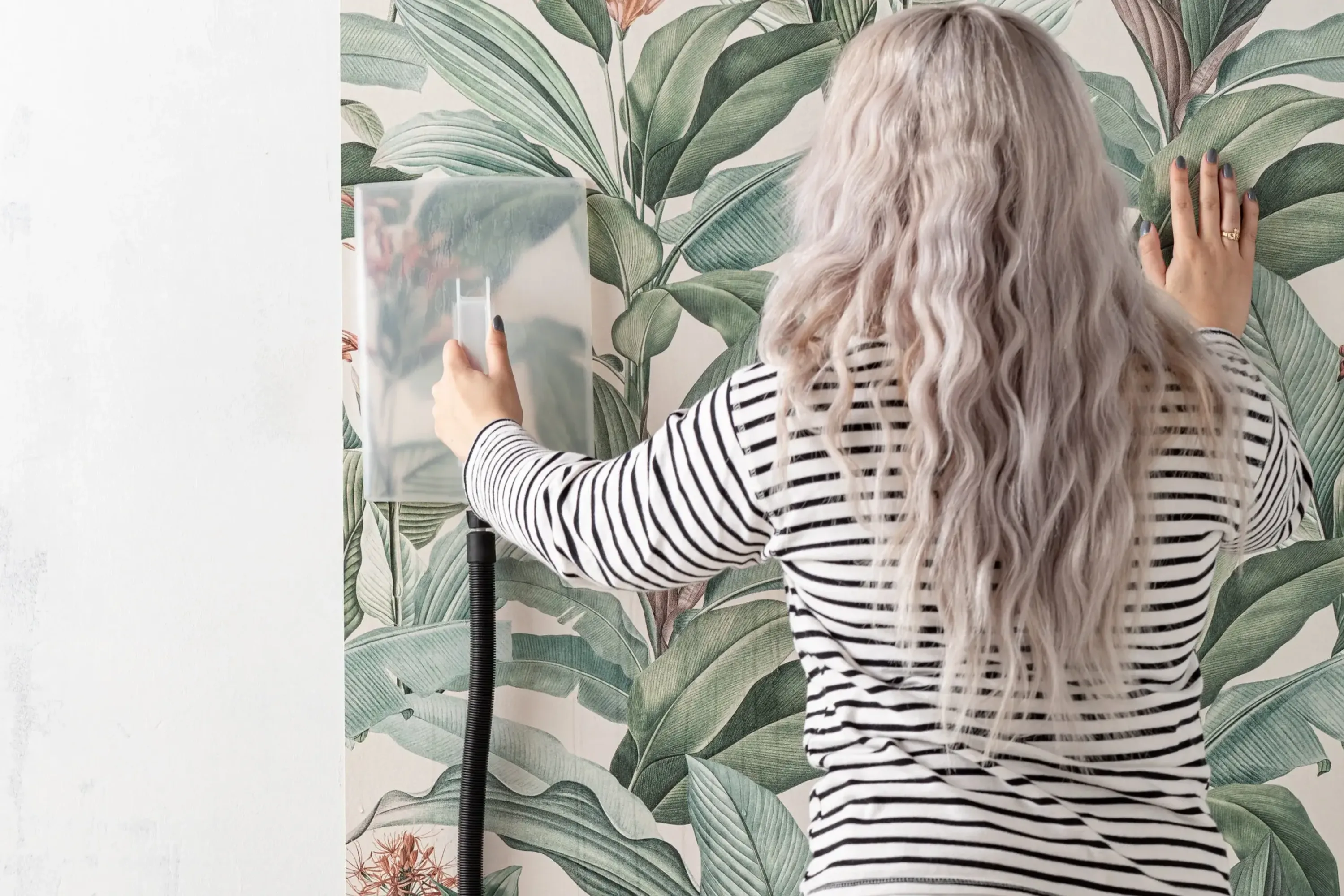 A woman uses a steamer to remove wallpaper from a wall.
