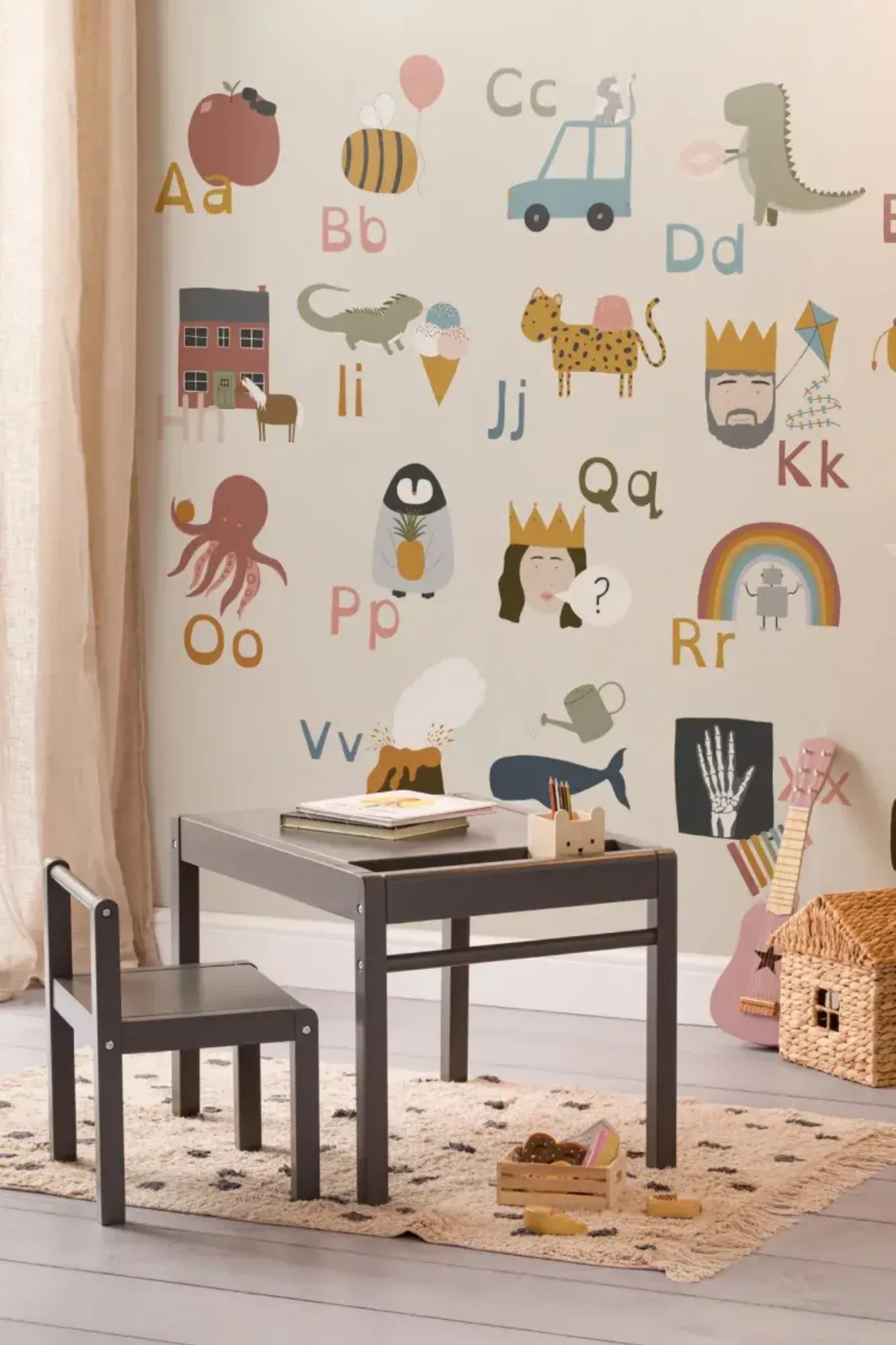 A children's playroom with a small table and chair set, featuring a colorful alphabet-themed mural with illustrations of various objects and animals corresponding to each letter of the alphabet.