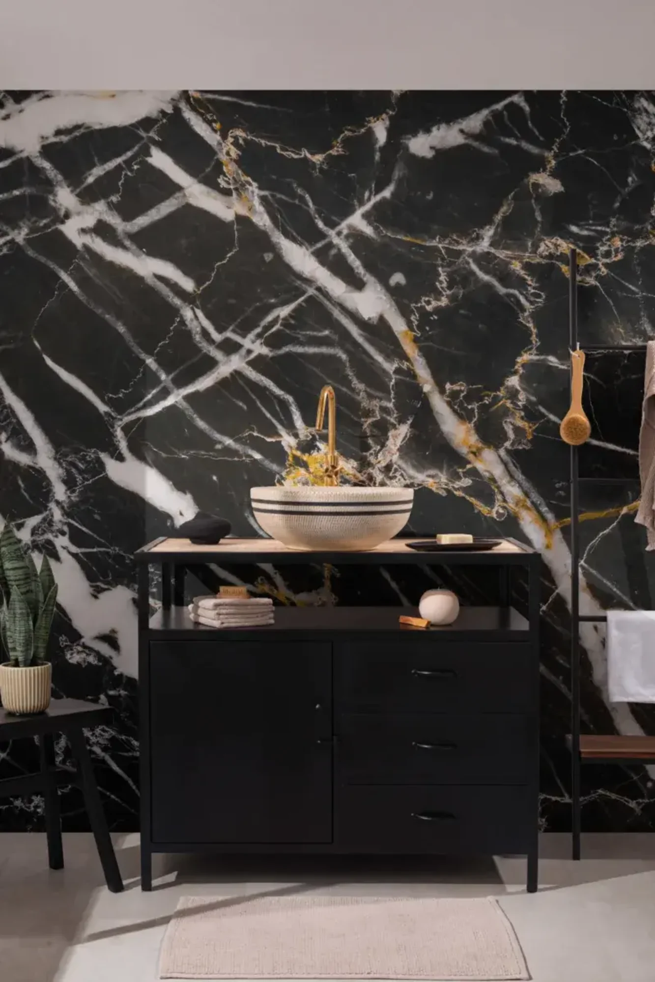 A modern bathroom with a black and white marble accent wall, a black vanity with a vessel sink, and gold fixtures.