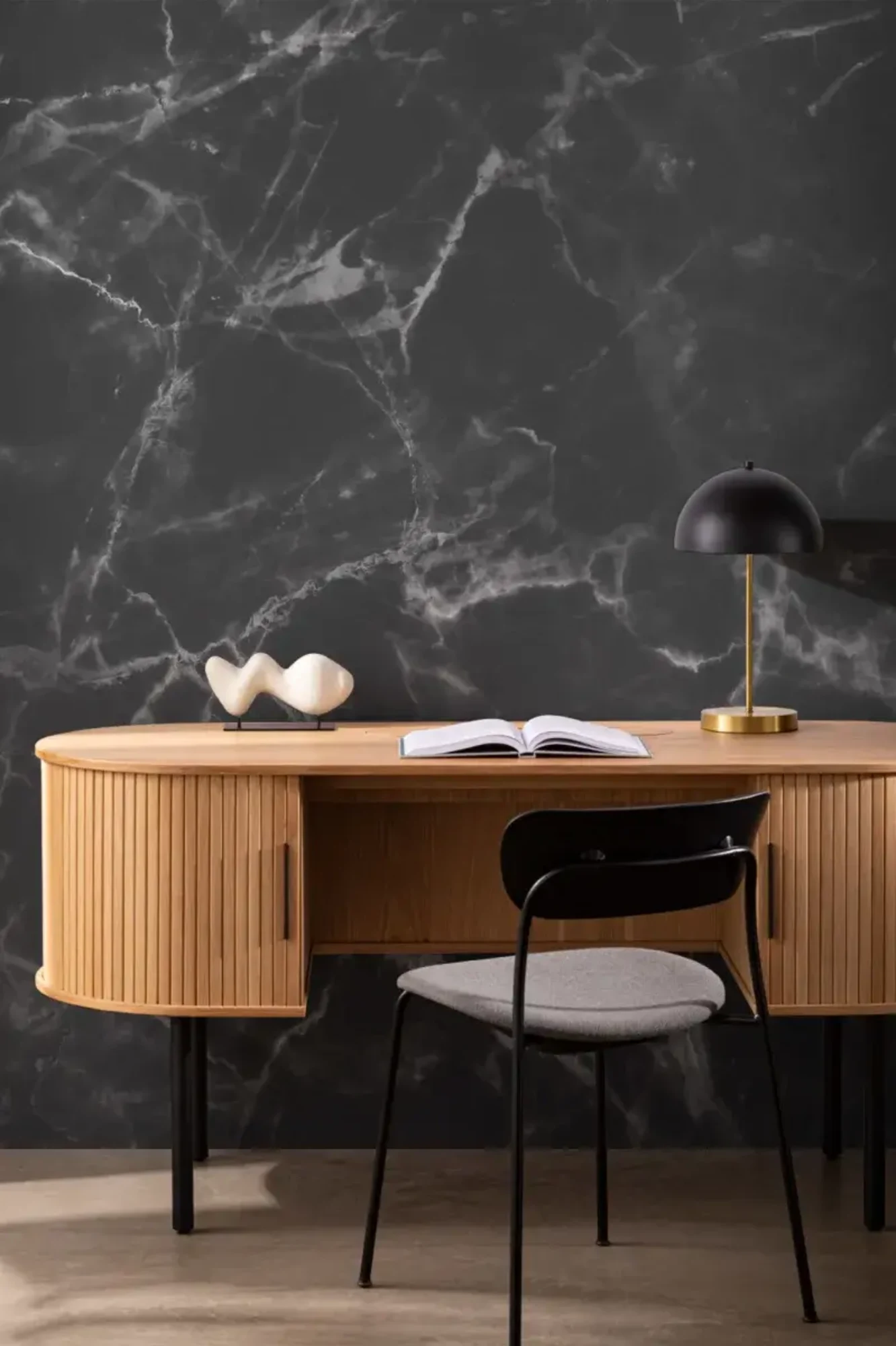 A modern office with a wooden desk, black chair, decorative sculpture, and lamp, set against a dark marble-patterned wallpaper background.