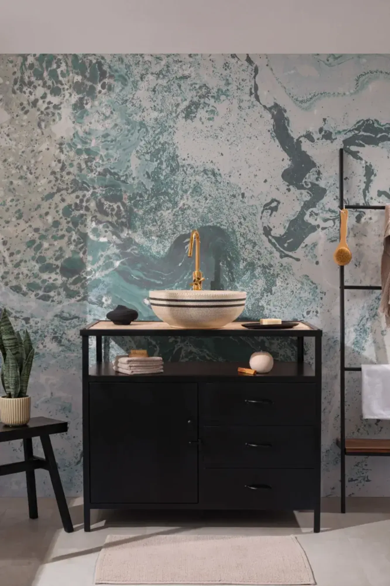  A modern bathroom with a black vanity, gold faucet, patterned sink, and a vibrant blue and green marbled wallpaper backdrop.