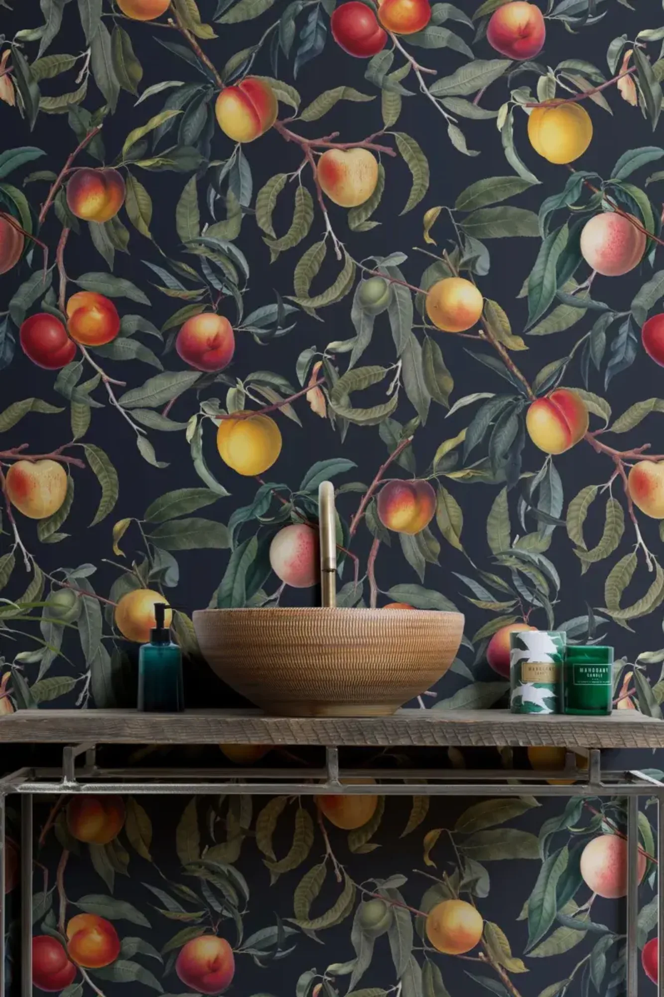 Luxurious bathroom featuring a woven vessel sink on a rustic metal vanity, accompanied by a blue soap dispenser and green candles, against a dark wall mural of peach branches with ripe fruits.