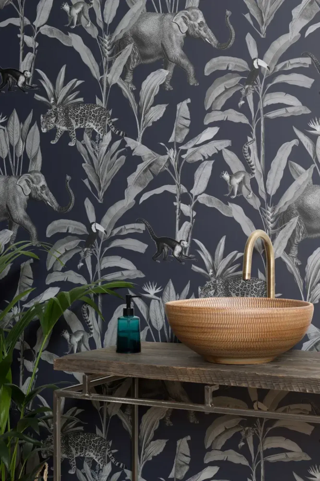 Exotic bathroom featuring a textured woven sink on a wooden vanity with a gold faucet, next to a blue soap dispenser, set against a dramatic wallpaper showcasing various jungle animals and lush foliage on a dark background.