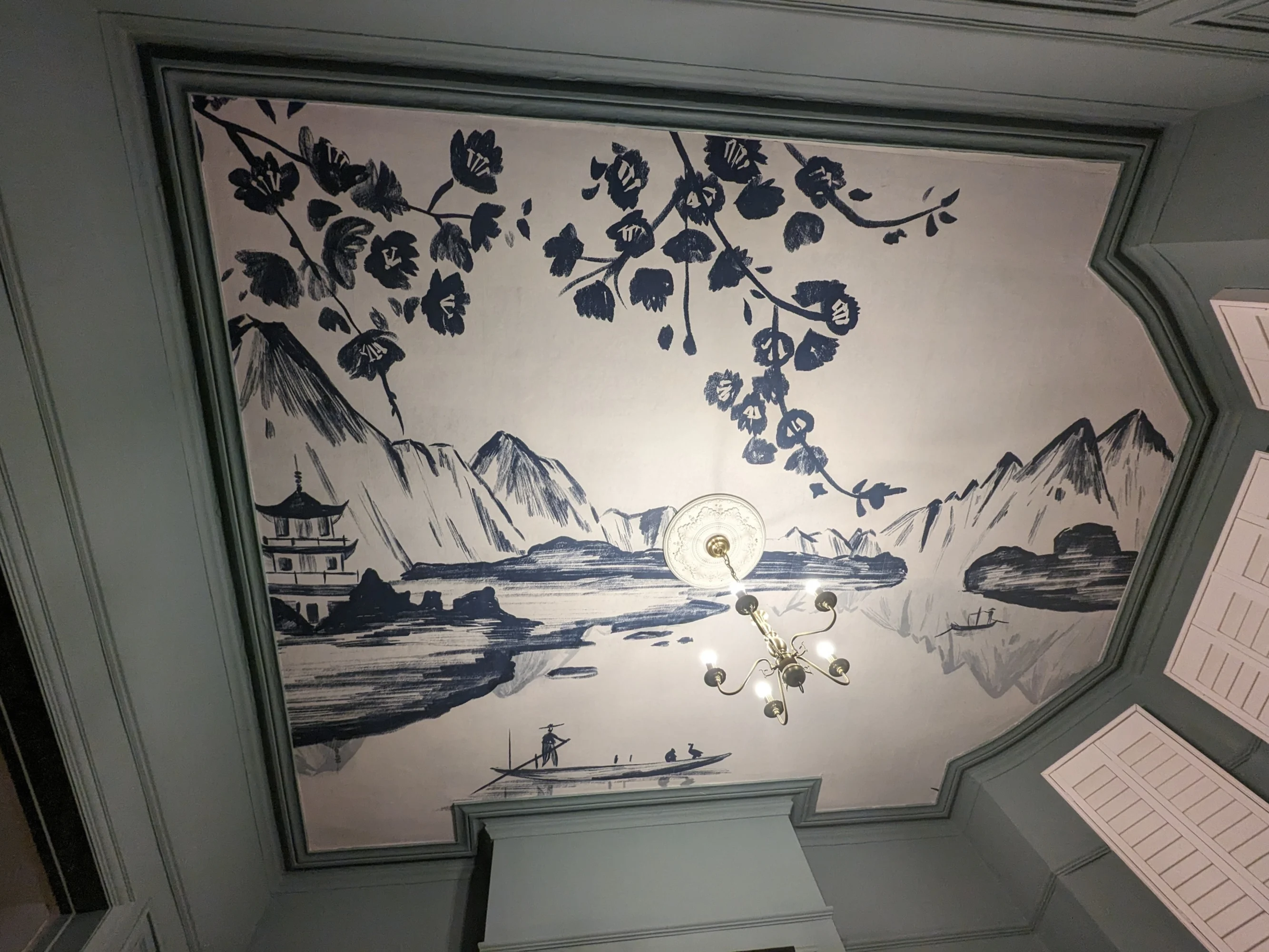 A ceiling mural in a room featuring an Asian landscape with mountains, a pagoda, and a river, with a central light fixture and surrounding blue-green trim.