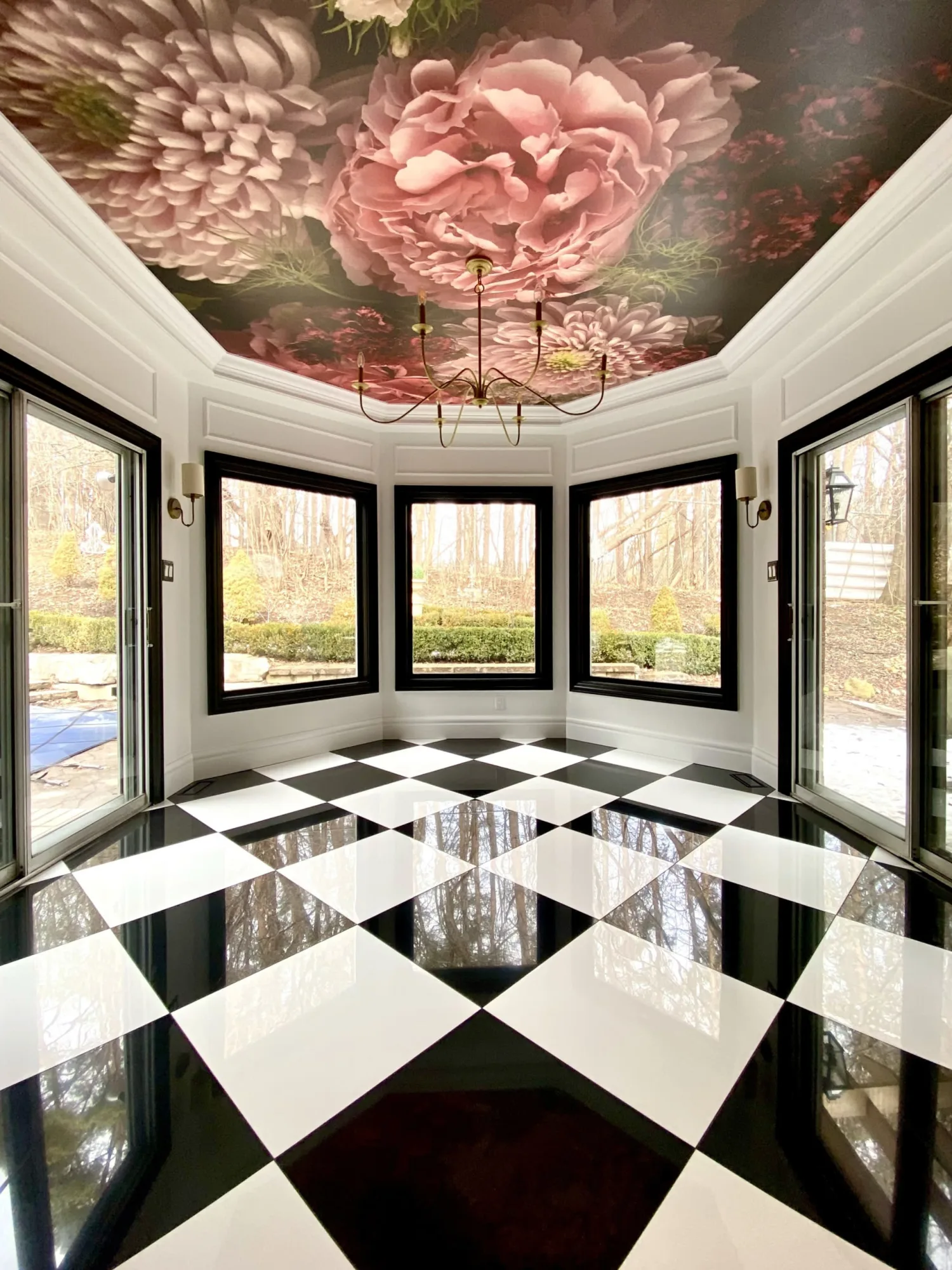 A sunroom with large windows, a black and white checkered floor, and a ceiling mural featuring large pink flowers.