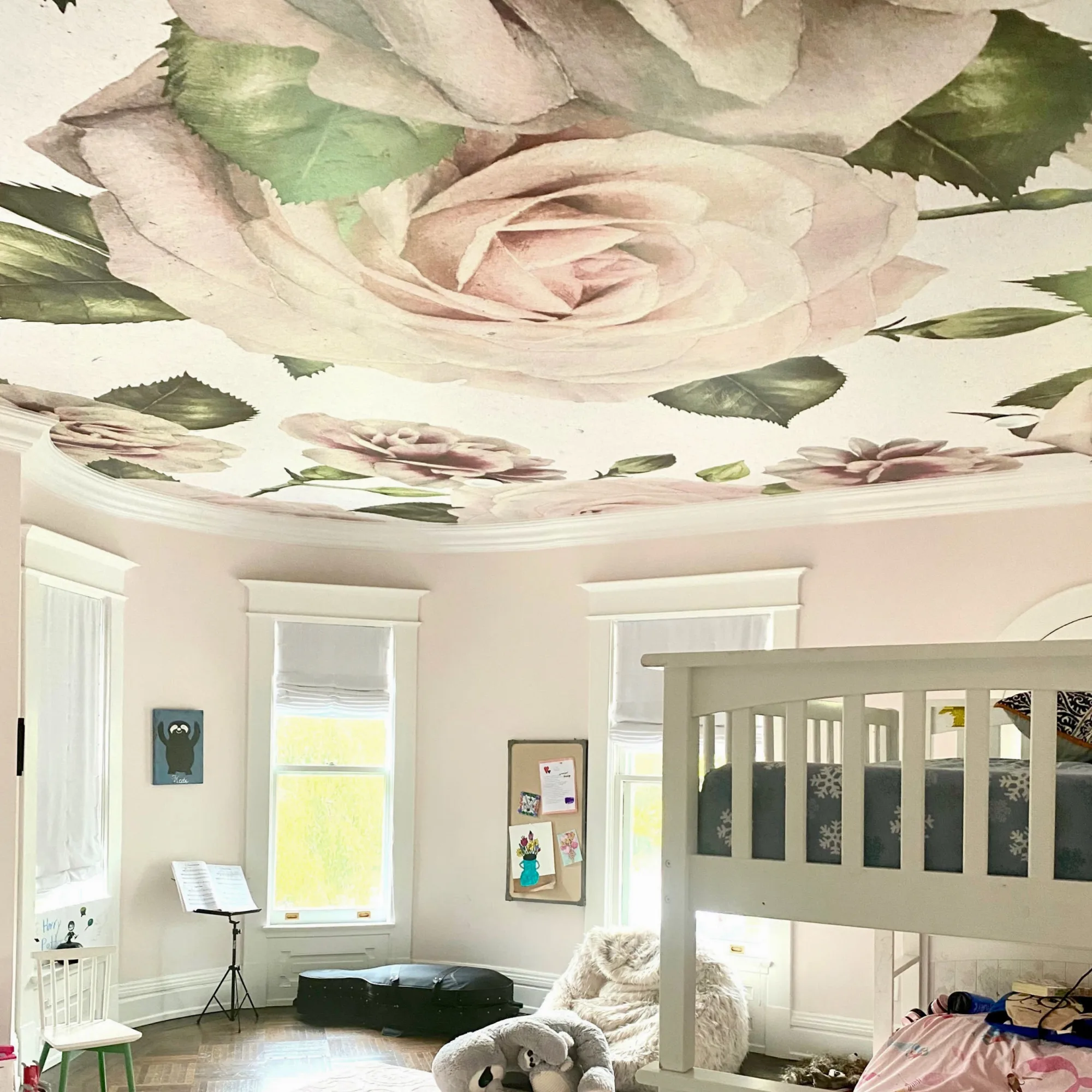 A children's bedroom with a large floral ceiling mural, a bunk bed, a music stand, a cozy chair, and large windows with white blinds.