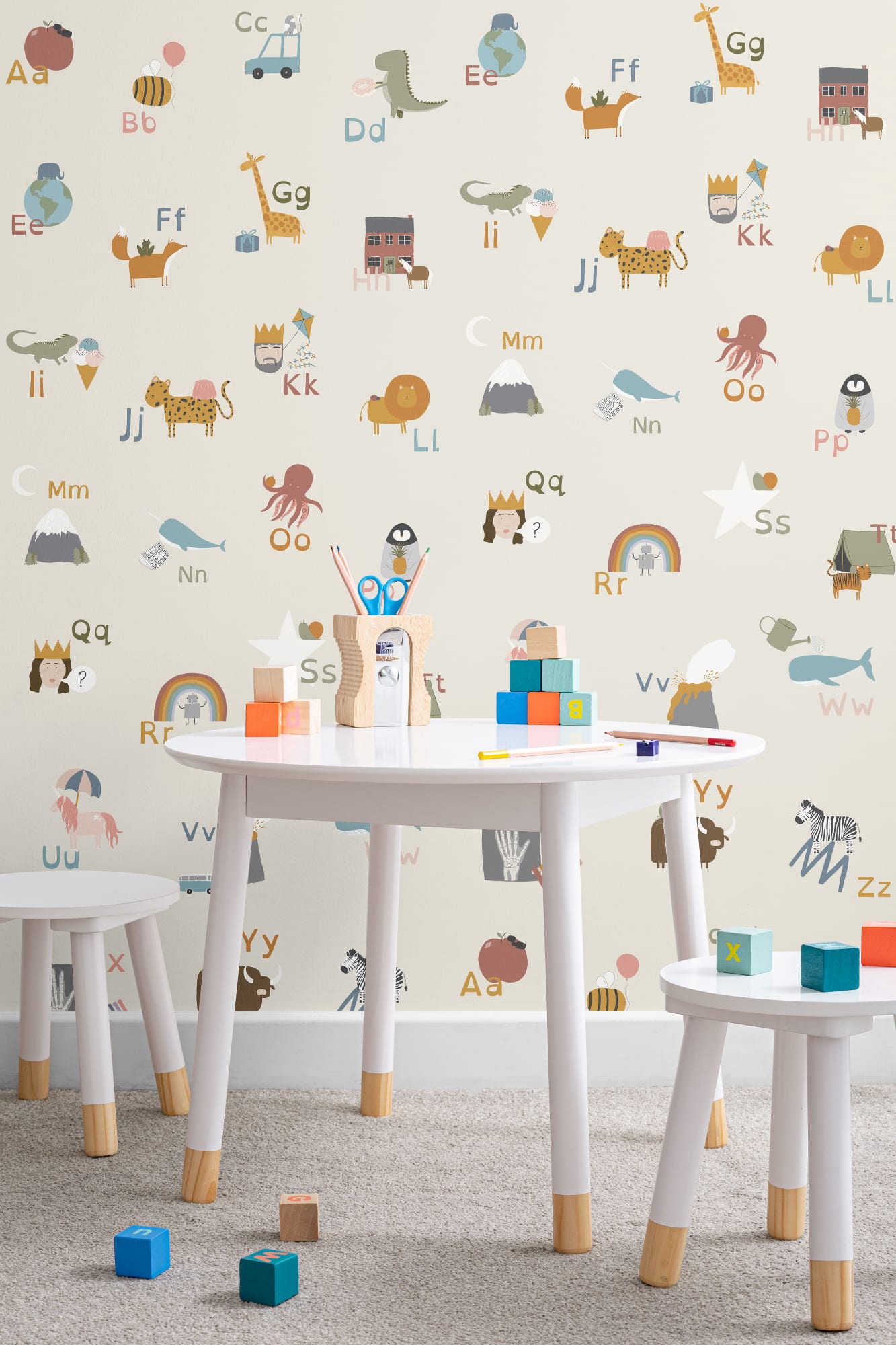 A fun, educational alphabet wallpaper with animal illustrations, complementing a kids' playroom with a table and building blocks.