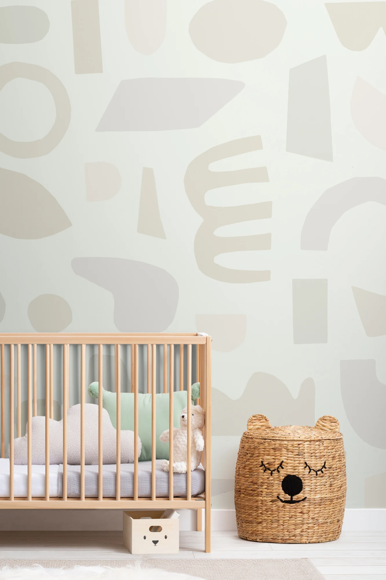 A pastel abstract wall mural with organic shapes, adding a gentle aesthetic to a nursery with a wooden crib and woven bear basket.